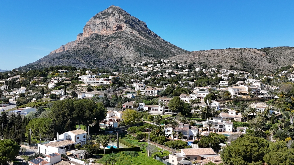 Vista panorámica del macizo del Montgó sobre el paisaje residencial de Jávea, destacando las villas blancas tradicionales y la exuberante vegetación mediterránea.