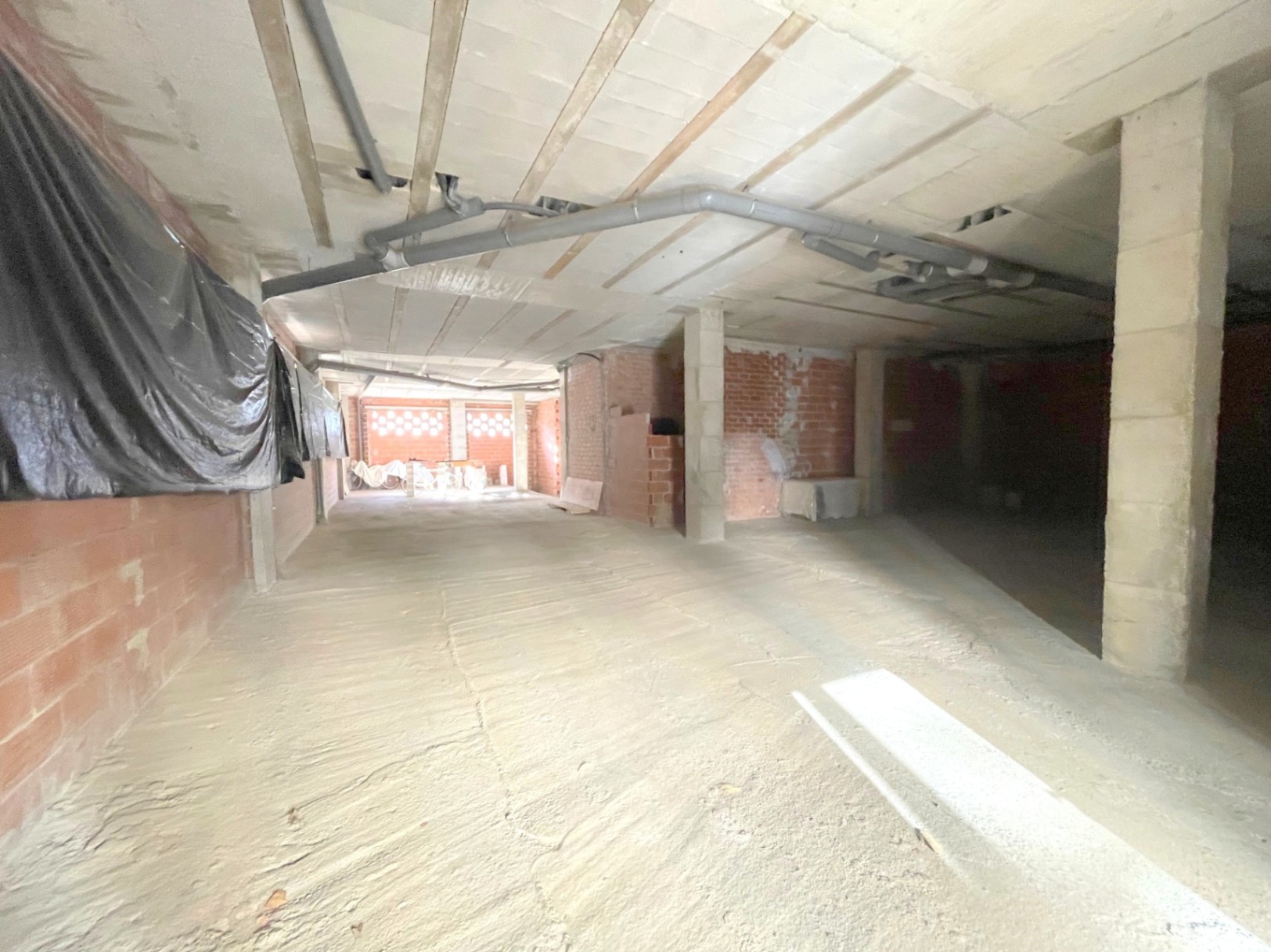 Local comercial diáfano en estado de obra con pilares de hormigón, techos altos con tuberías vistas y muros de ladrillo que permiten una distribución flexible.