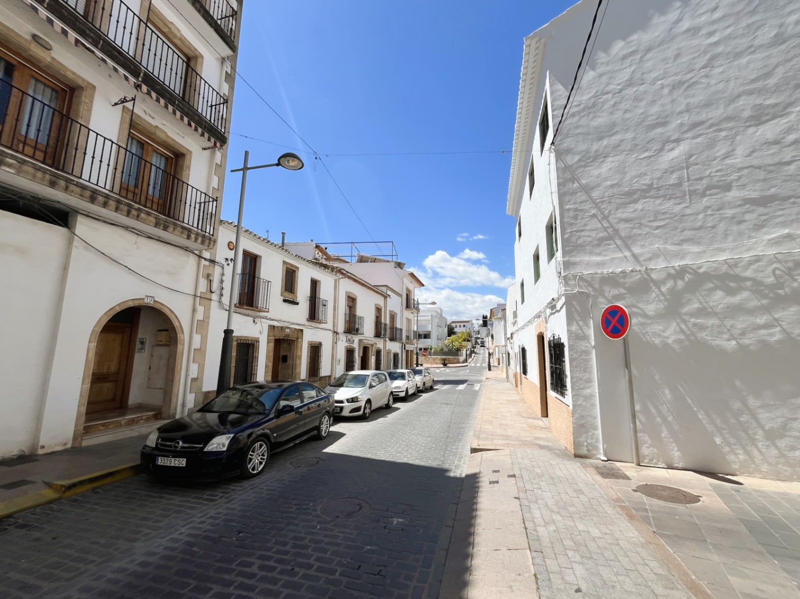 Fachada exterior del edificio situada en una calle empedrada del casco antiguo de Jávea, con arcos de piedra tosca y balcones tradicionales de hierro forjado.