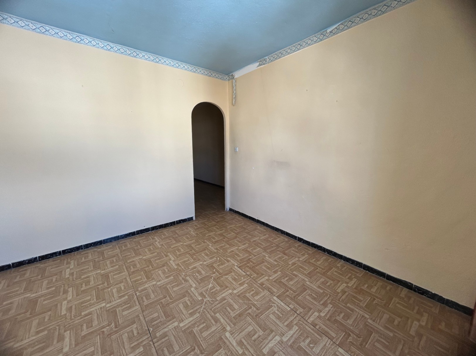 Habitación interior con suelos de gres cerámico estampado, paredes en tono crema y un techo azul con cenefa decorativa. Destaca el acceso mediante un arco de medio punto.