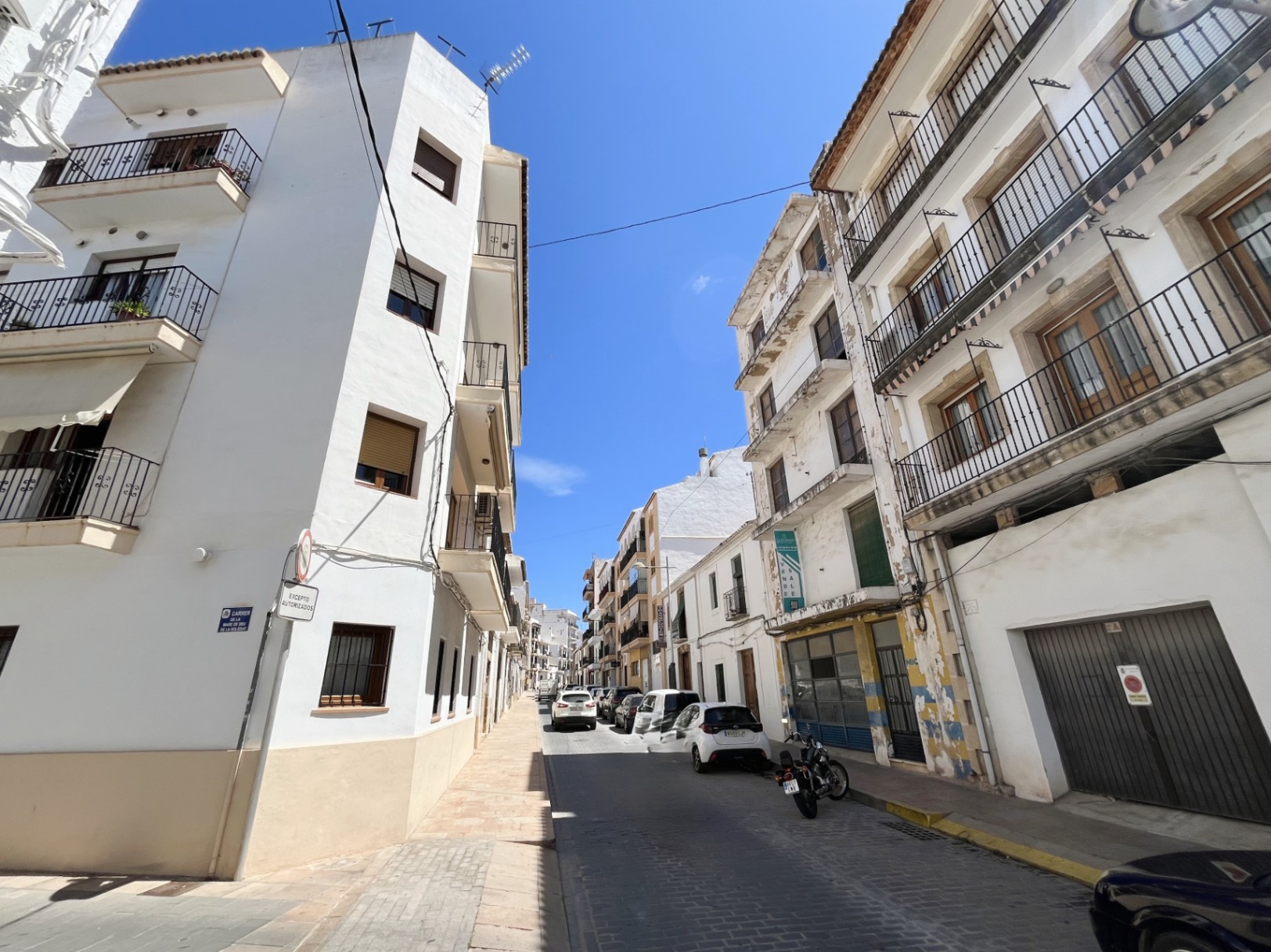 Vista exterior del edificio de cuatro plantas en el casco urbano de Jávea, destacando su fachada blanca con balcones de forja y el amplio local comercial en la planta baja.