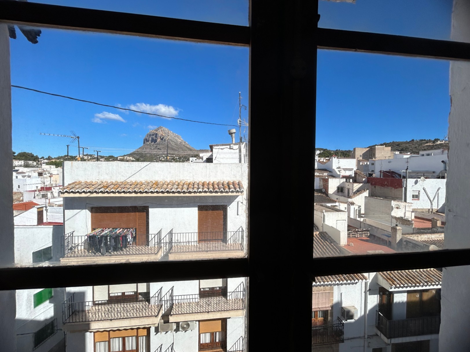 Vista urbana desde el interior a través de un ventanal, mostrando los tejados del casco antiguo de Jávea y la silueta del macizo del Montgó bajo un cielo despejado.