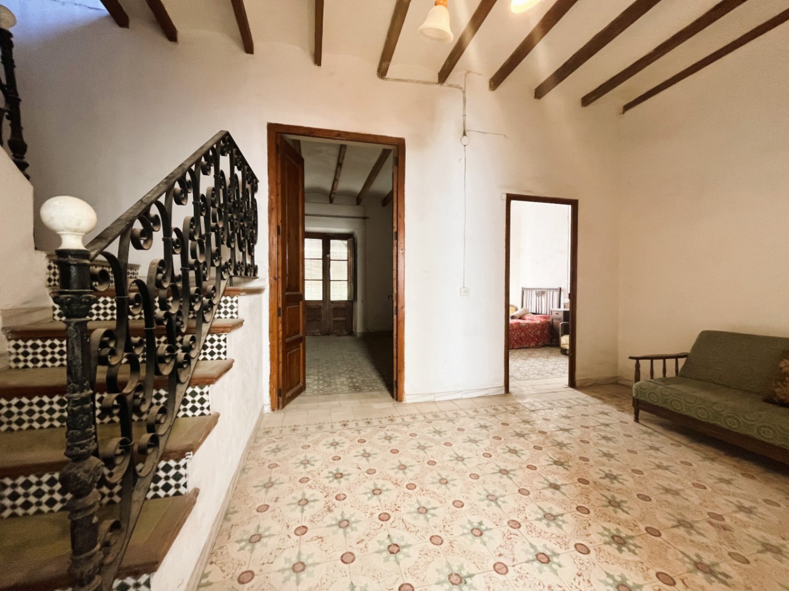 Distribuidor con suelos hidráulicos originales, vigas de madera vista y una escalera señorial con barandilla de hierro forjado artesanal.