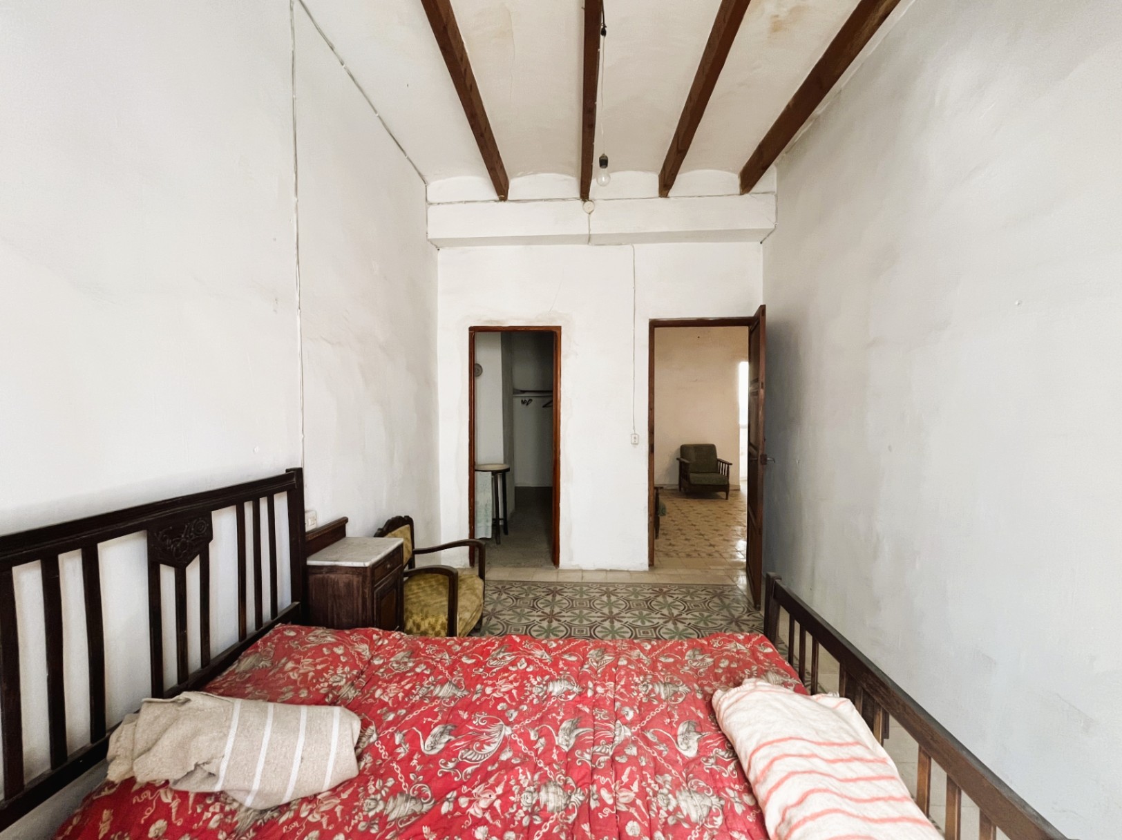 Dormitorio con techos altos y vigas de madera vista, suelos de baldosa hidráulica original y mobiliario de época, con acceso a estancias contiguas.