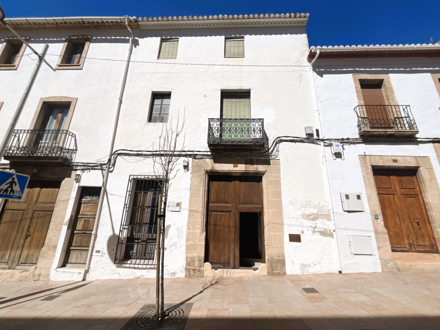 Fachada tradicional con muros de cal blanca, gran portón de madera enmarcado en piedra tosca y balcones de hierro forjado en el casco antiguo.