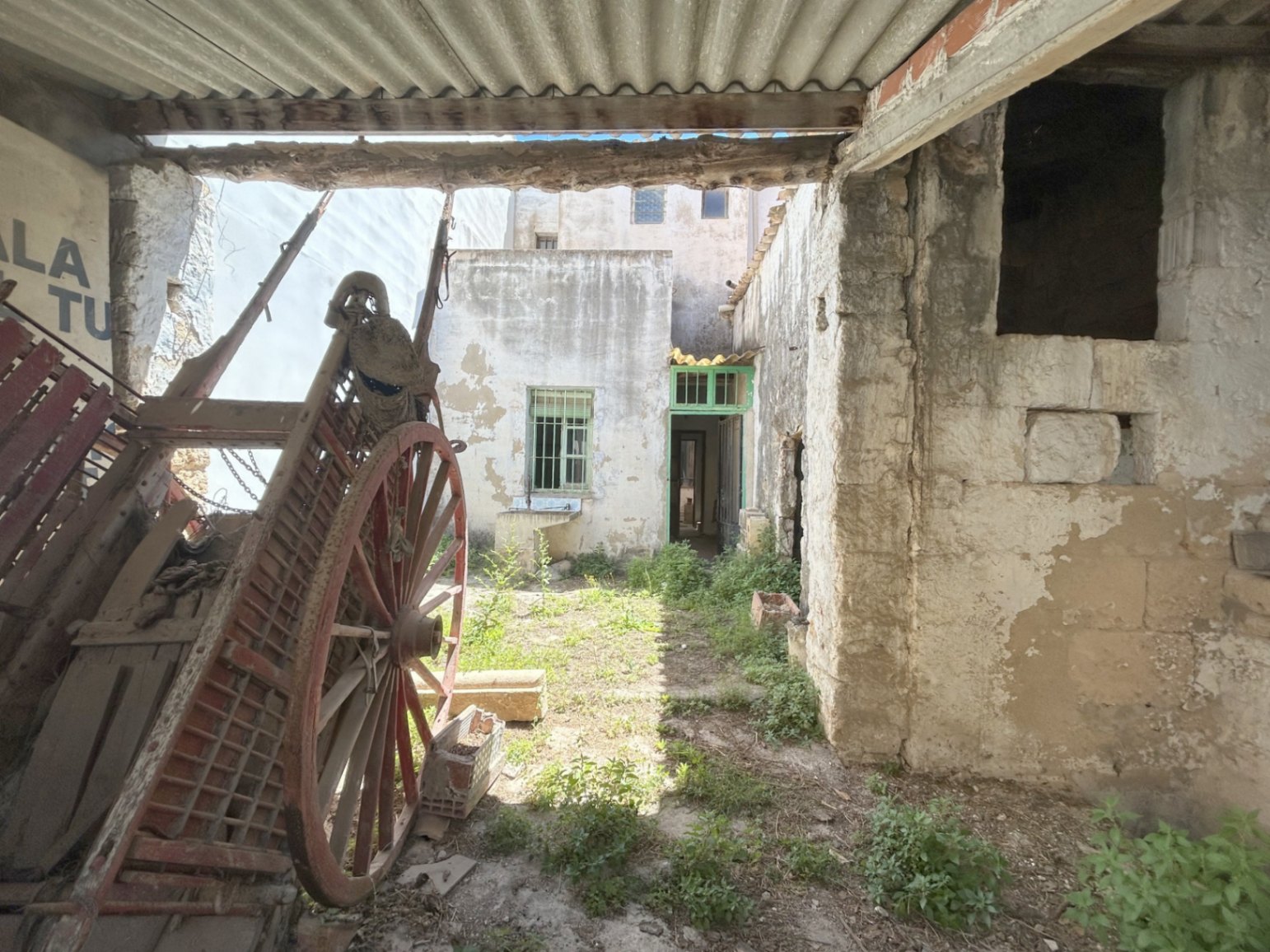Patio trasero con carro antiguo de madera y muros de piedra original. Espacio exterior con acceso independiente y gran potencial de rehabilitación.