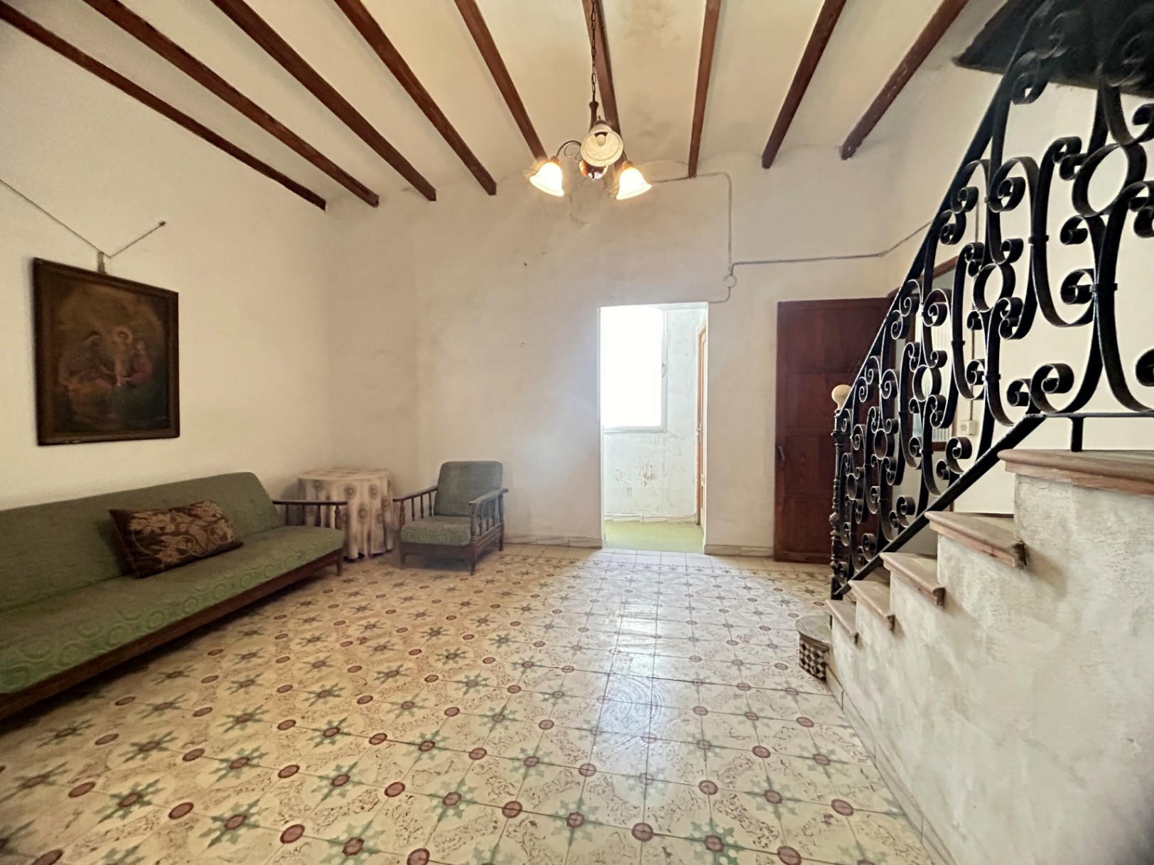 Salón señorial con suelos hidráulicos originales, techos altos con vigas de madera vista y una escalera con barandilla de hierro forjado artesanal.