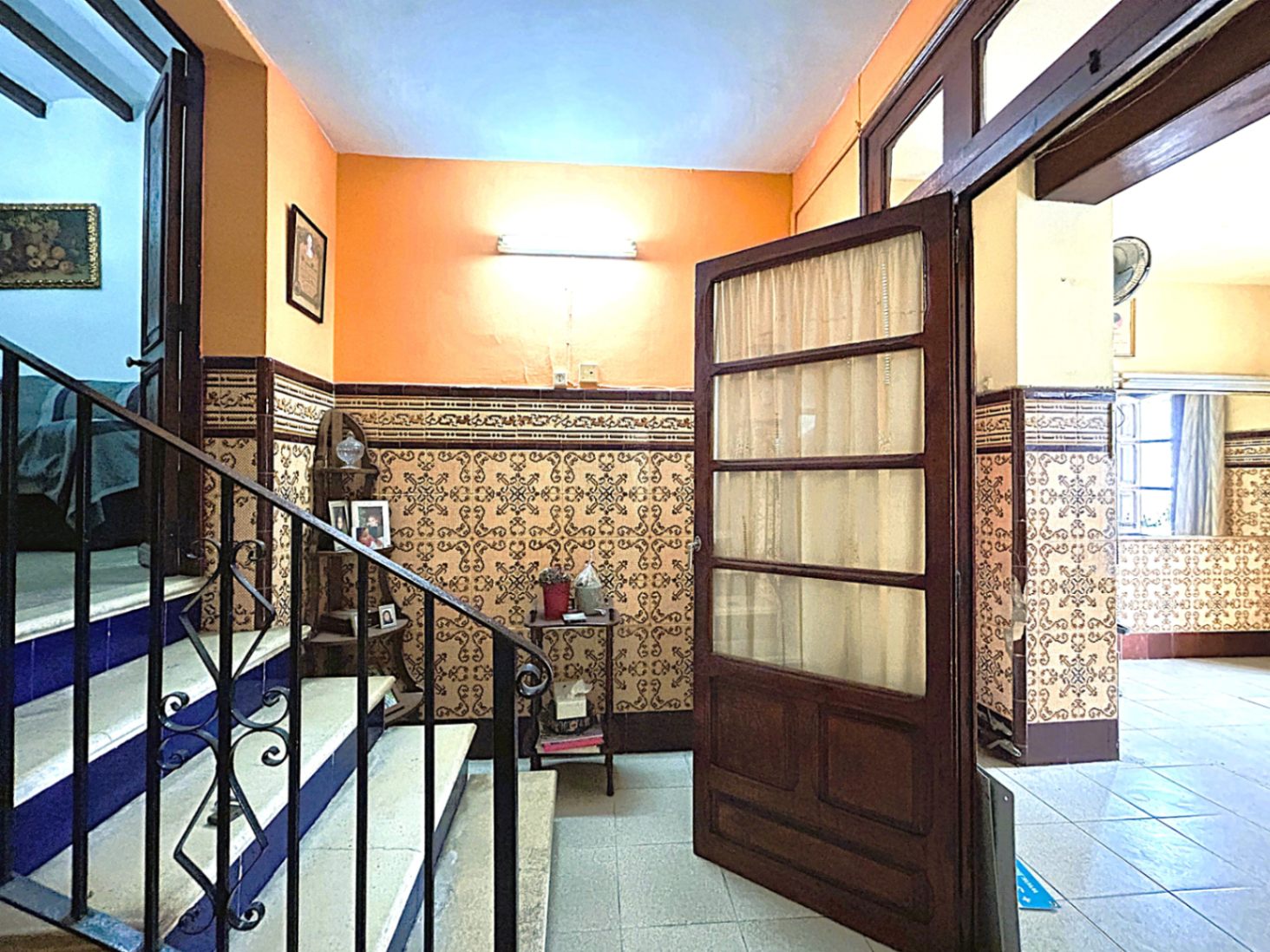 Entrada tradicional con zócalos de azulejos decorativos, escalera de piedra con contrahuellas azules y barandilla de hierro forjado en el casco antiguo.