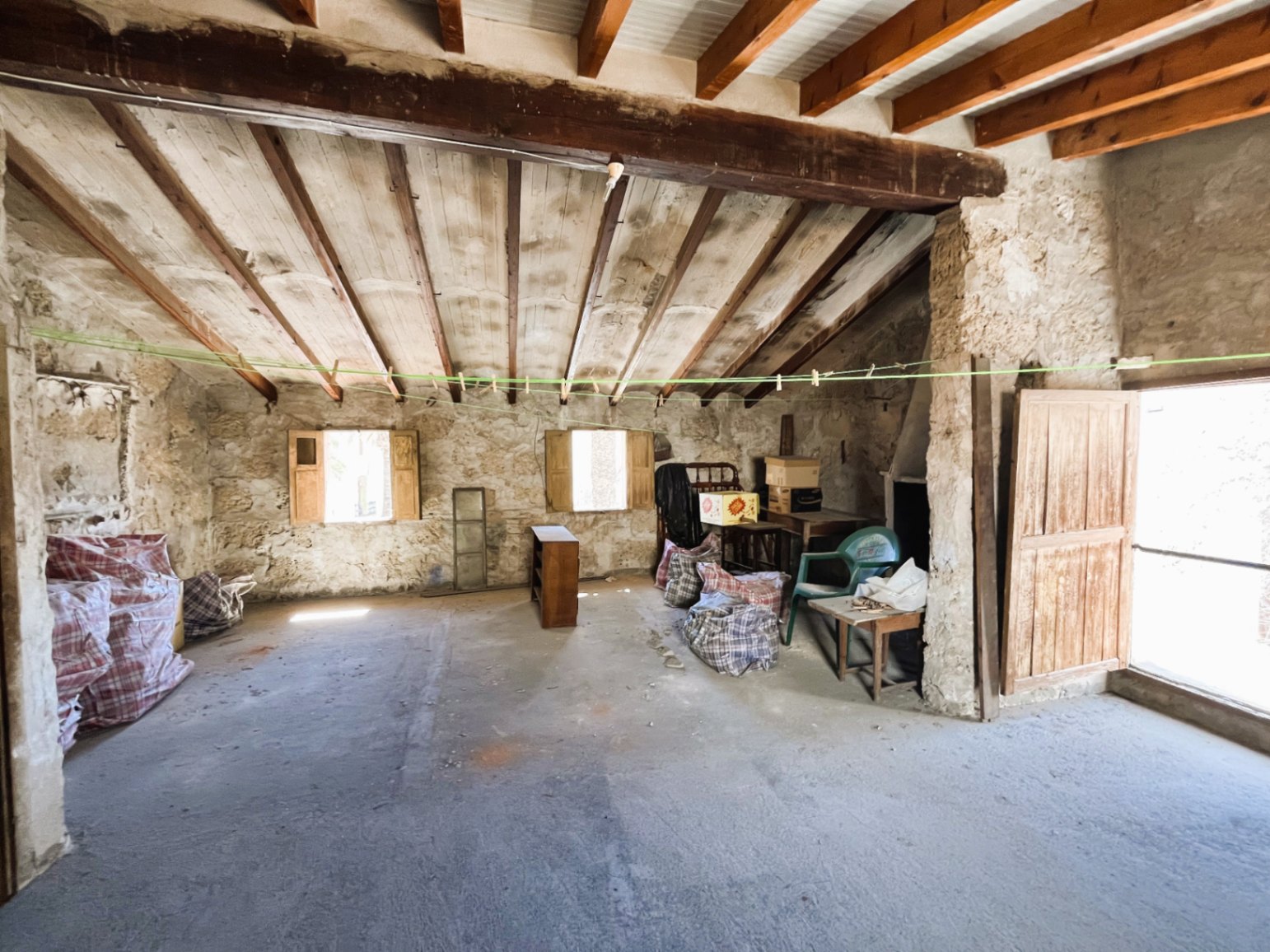 Espaciosa buhardilla con vigas de madera y muros de piedra natural, destacando por su estructura de techo inclinado y gran potencial para una reforma integral.