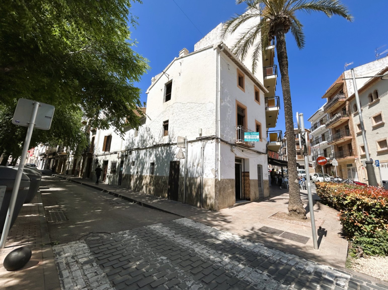 Fachada exterior de esquina en el casco antiguo de Jávea, mostrando tres plantas con balcones y carpintería de madera tradicional bajo un cielo despejado.