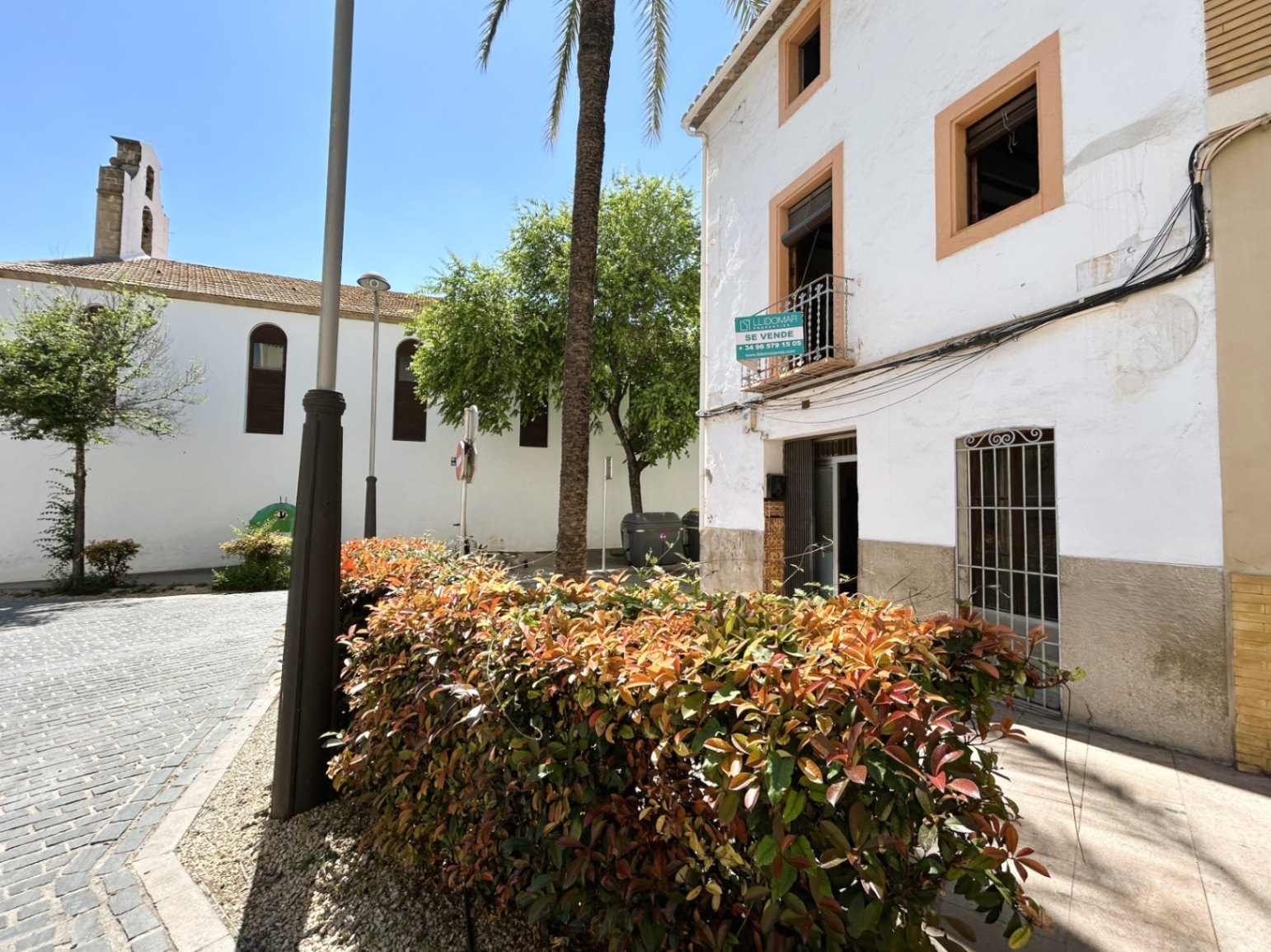 Fachada tradicional blanca con marcos ocre, situada en una plaza empedrada junto a una iglesia histórica en el casco antiguo de Jávea.