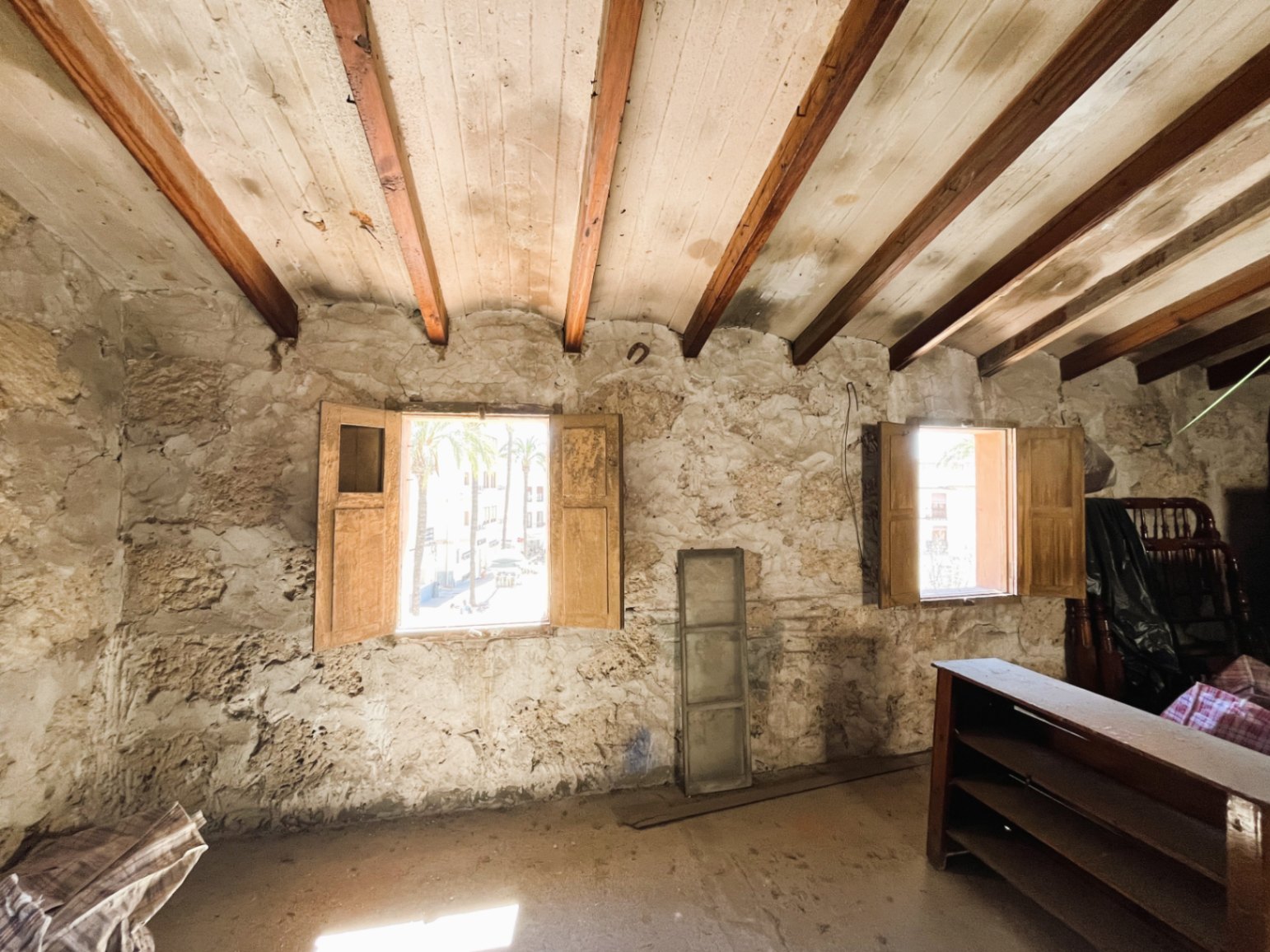 Habitación con muros de piedra natural vista y techos de vigas de madera originales. Dos ventanas con contraventanas de madera ofrecen vistas al casco antiguo y luz natural.