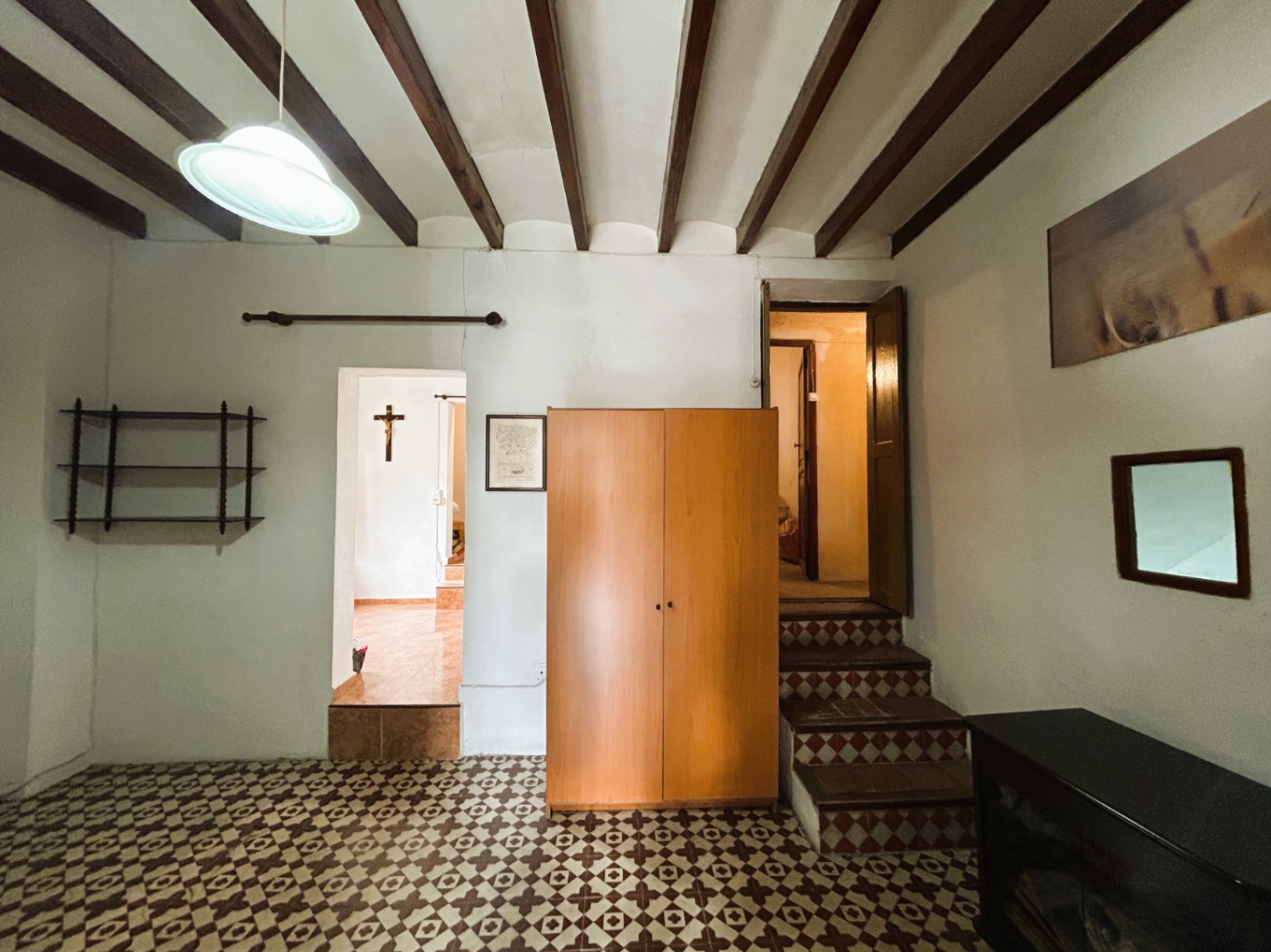 Habitación con vigas de madera vistas, suelos de mosaico hidráulico original y acceso a niveles superiores mediante escaleras con azulejos geométricos.