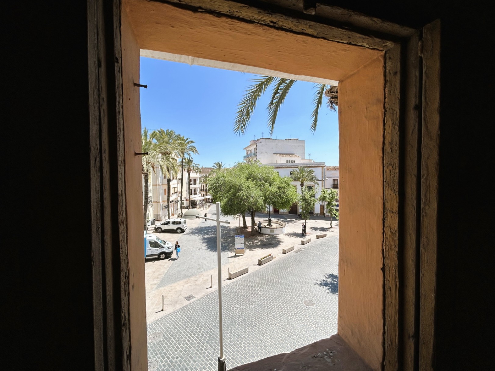 Vista desde el interior hacia una plaza empedrada en el casco antiguo, resaltando el grosor de los muros tradicionales y la luminosidad exterior con palmeras.