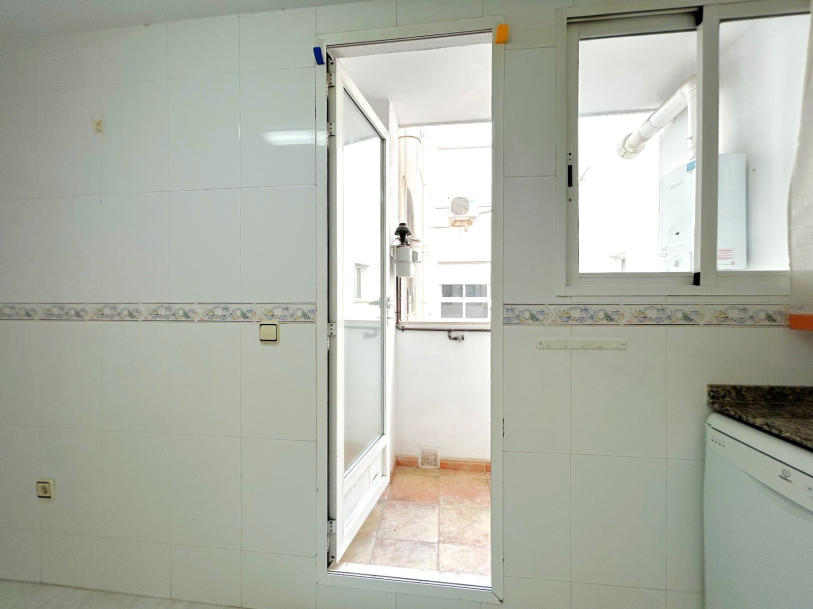 Galería exterior accesible desde la cocina, con paredes alicatadas en blanco, encimera de granito y zona para lavadero con calentador de agua.