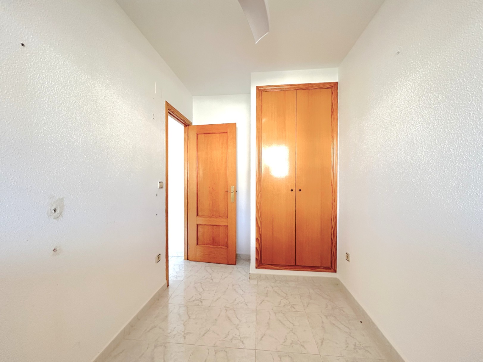 Pasillo de distribución con suelos de gres cerámico efecto mármol, paredes blancas y armario empotrado de madera natural integrado.