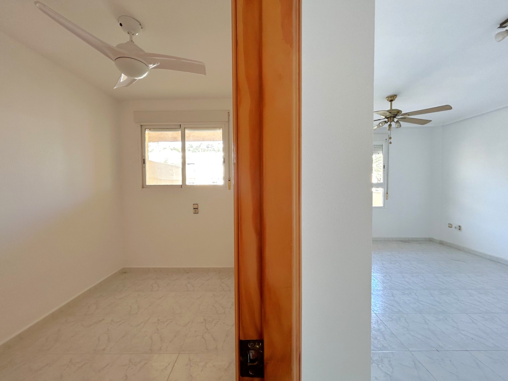 Vista de dos dormitorios contiguos con suelos de gres, ventiladores de techo y carpintería interior de madera natural.