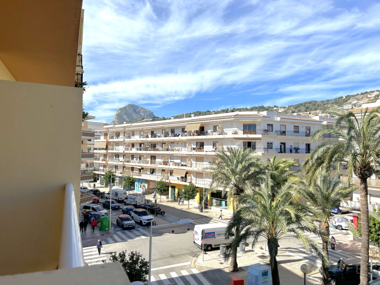 Vistas despejadas desde el balcón hacia el centro del Puerto de Jávea, con la emblemática montaña del Montgó al fondo y calles arboladas con palmeras mediterráneas.