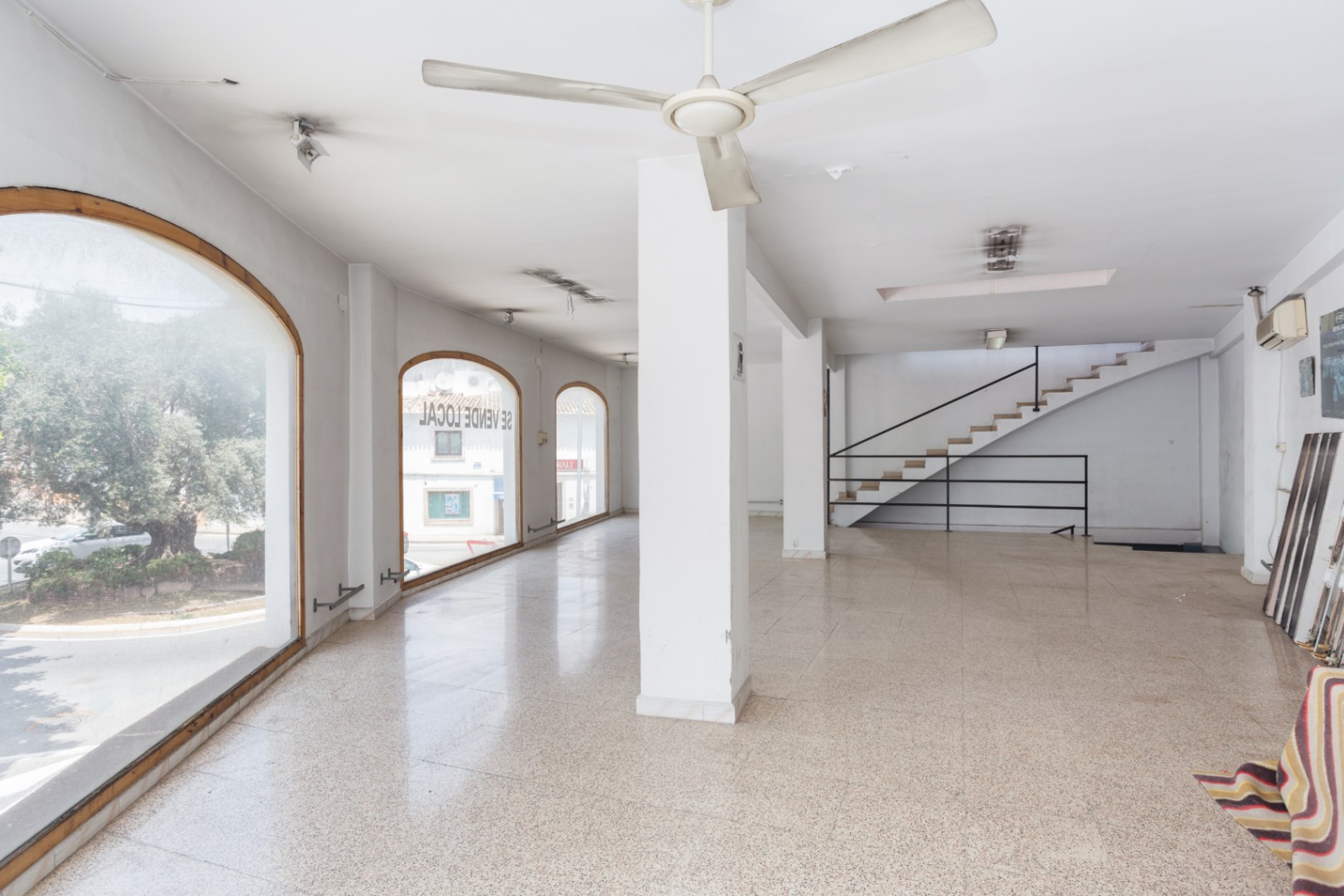 Planta principal diáfana con amplios ventanales en arco, suelos de terrazo y escalera de acceso a la planta superior con barandilla metálica negra.
