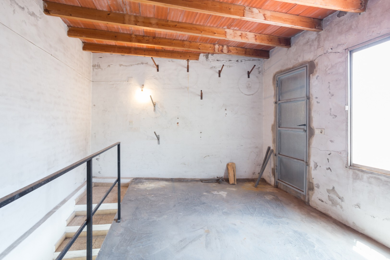 Planta superior con techos de vigas de madera y bovedillas cerámicas. Incluye acceso por escalera con barandilla metálica, suelos de cemento y carpintería metálica industrial.