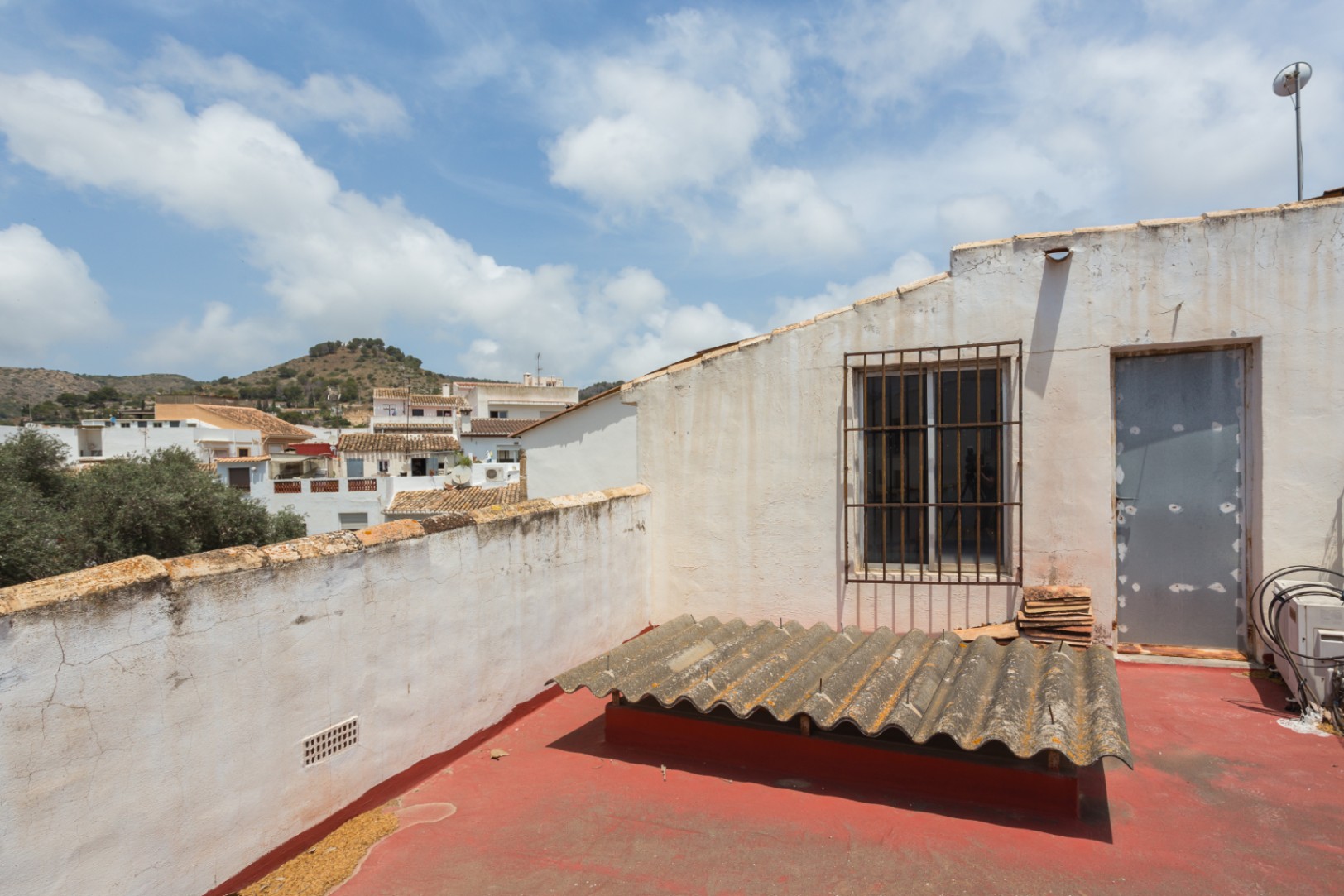 Terraza superior con suelo de pintura roja y vistas despejadas al entorno urbano y las montañas de Jávea. Incluye acceso directo y un lucernario protegido.