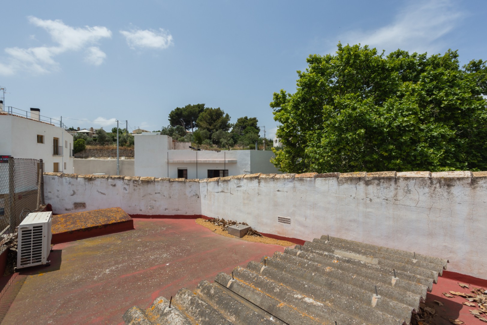 Terraza superior con suelo rojizo y muros perimetrales blancos, ofreciendo vistas despejadas al entorno urbano y vegetación mediterránea en Jávea.