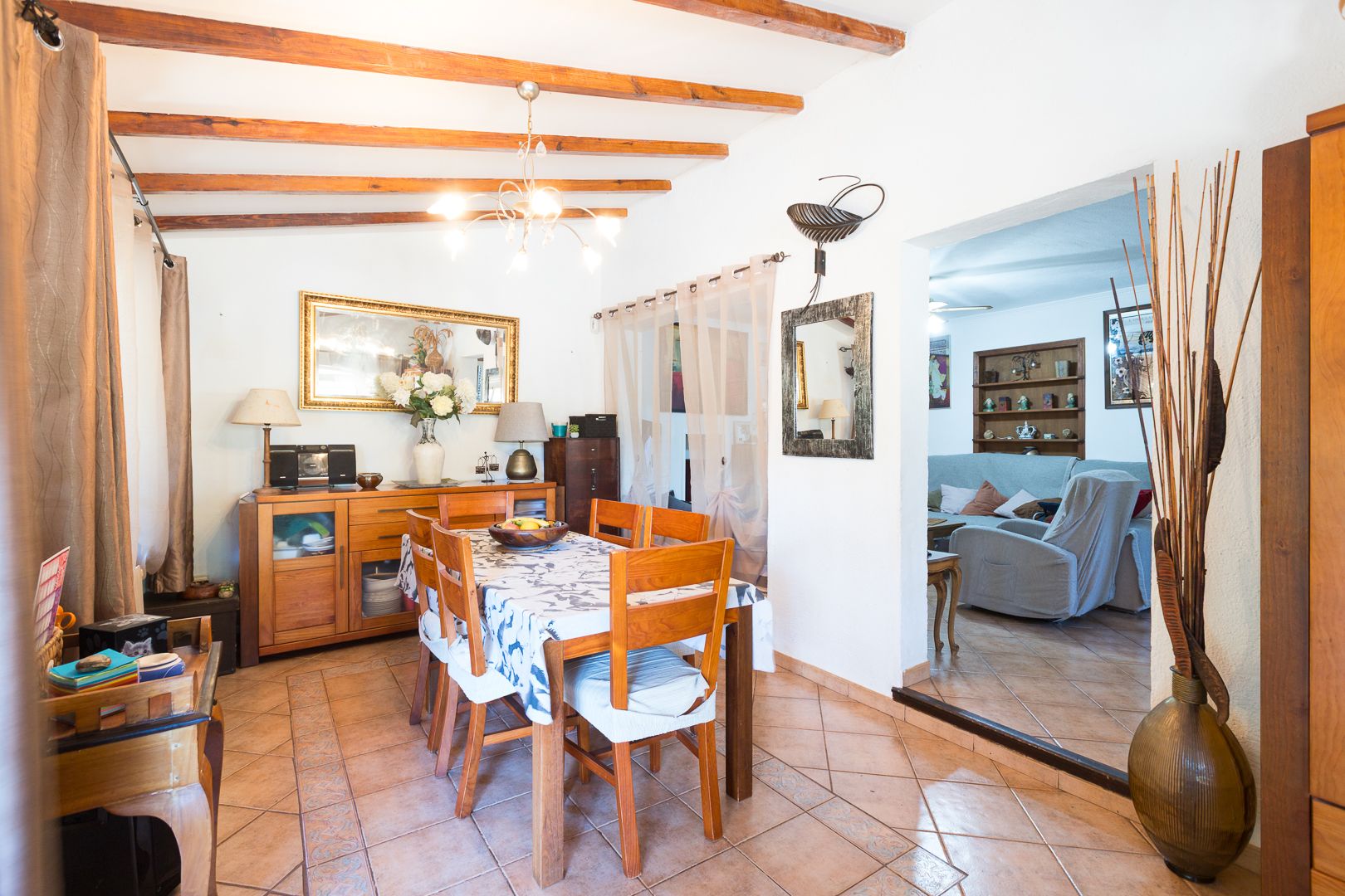 Comedor rústico con vigas de madera a la vista, suelos de gres cerámico y mobiliario de madera maciza conectado visualmente con el salón.