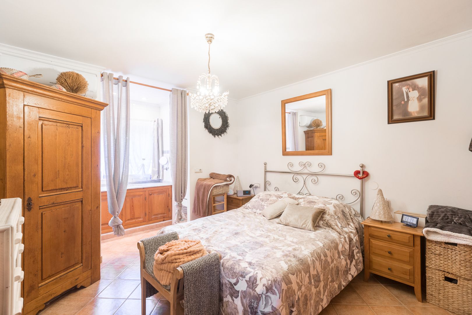 Dormitorio con suelos cerámicos, armario de madera clásica y cabecero de forja. Dispone de aire acondicionado, lámpara de araña y ventanal con luz natural.