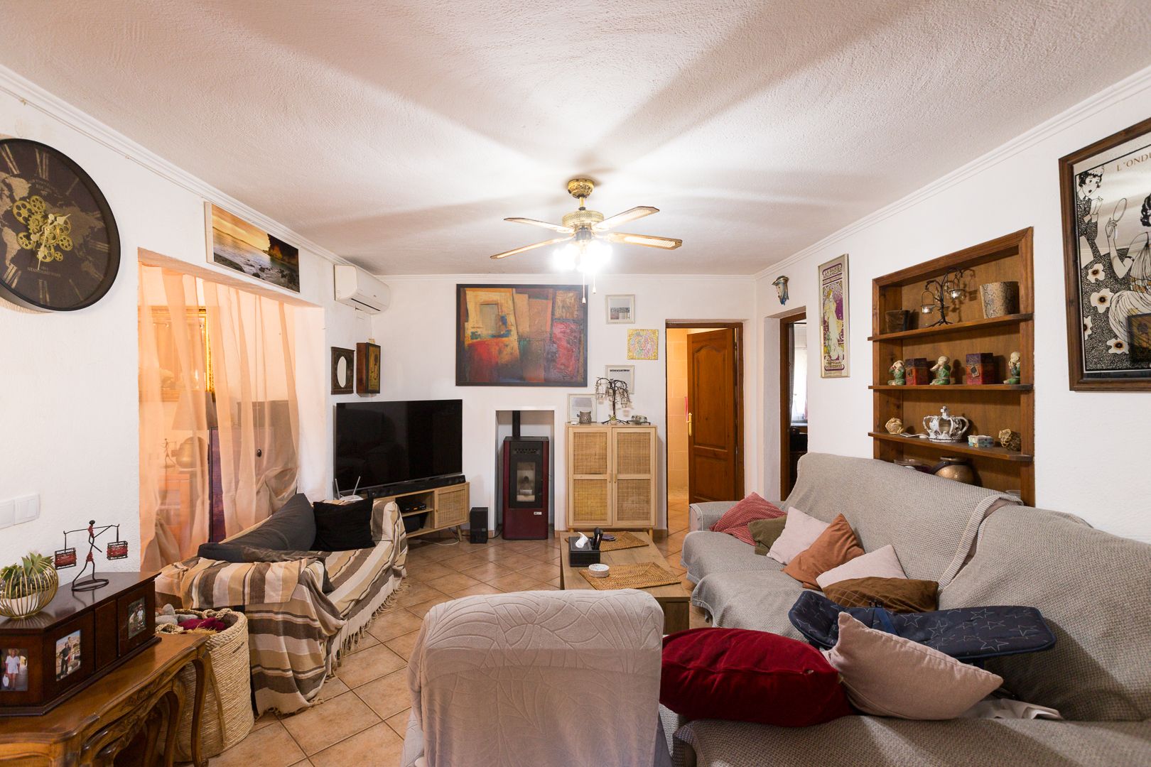 Salón acogedor con suelos de gres, estufa de pellets, aire acondicionado y ventilador de techo. Incluye estanterías de madera integradas y acceso a las estancias interiores.