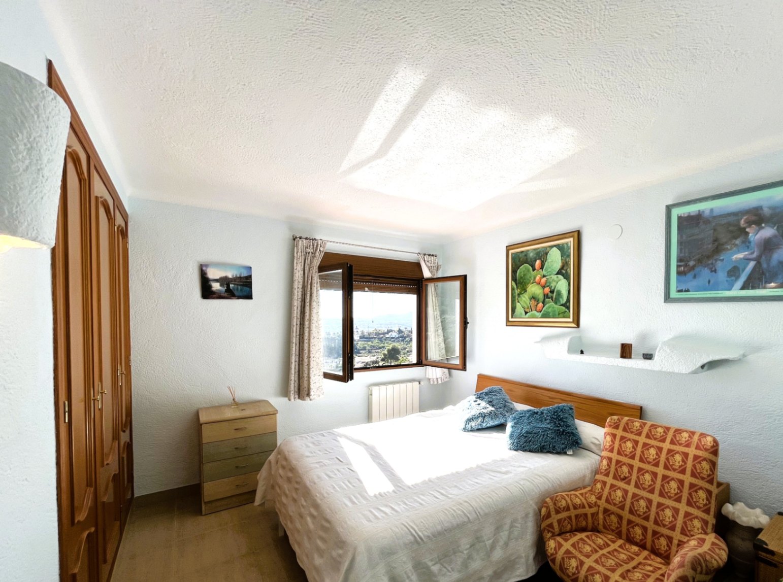 Dormitorio con armarios empotrados de madera, cama doble y ventana con vistas panorámicas al valle, destacando por su abundante luz natural.