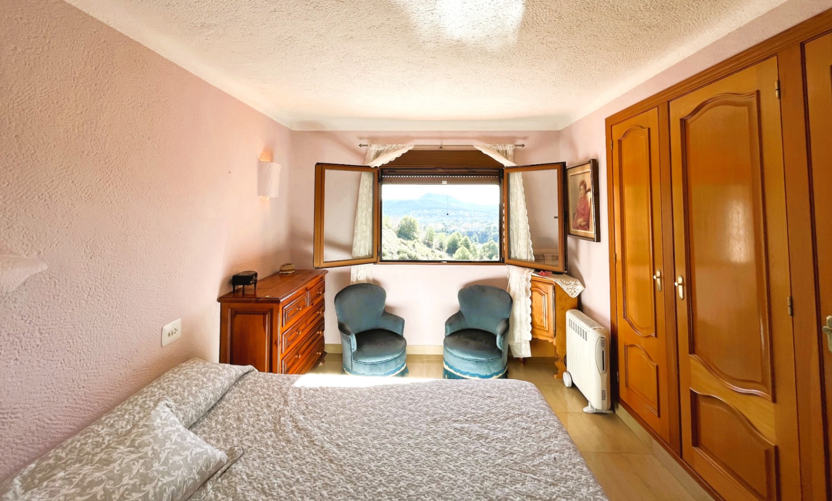 Dormitorio con paredes de textura malva, armarios empotrados de madera y ventana con vistas despejadas al entorno natural del Montgó.