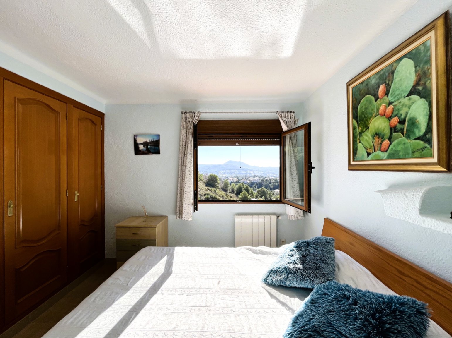 Dormitorio luminoso con armario empotrado de madera, calefacción por radiador y ventana abierta con vistas panorámicas a las montañas y el entorno natural del Montgó.