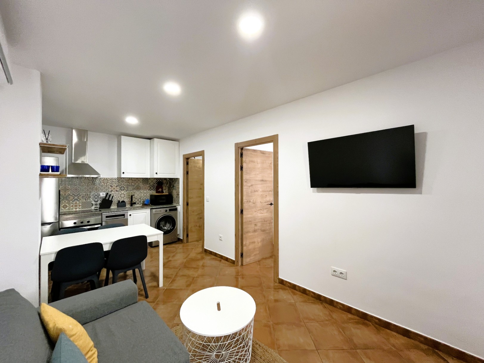 Salón-comedor integrado con cocina reformada, salpicadero de azulejo hidráulico, iluminación empotrada y suelos de gres en tonos cálidos.