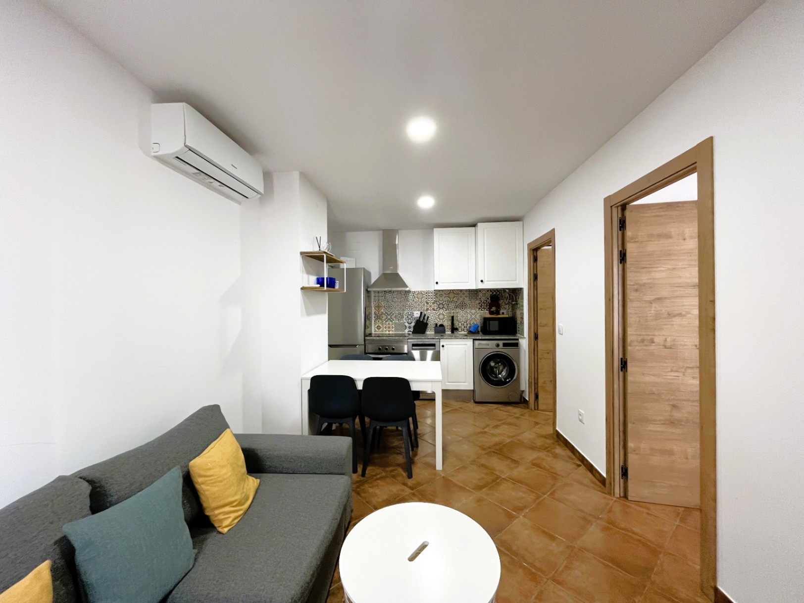 Zona de estar y cocina integrada con frente de azulejos hidráulicos, aire acondicionado tipo split y suelos cerámicos de estilo rústico.