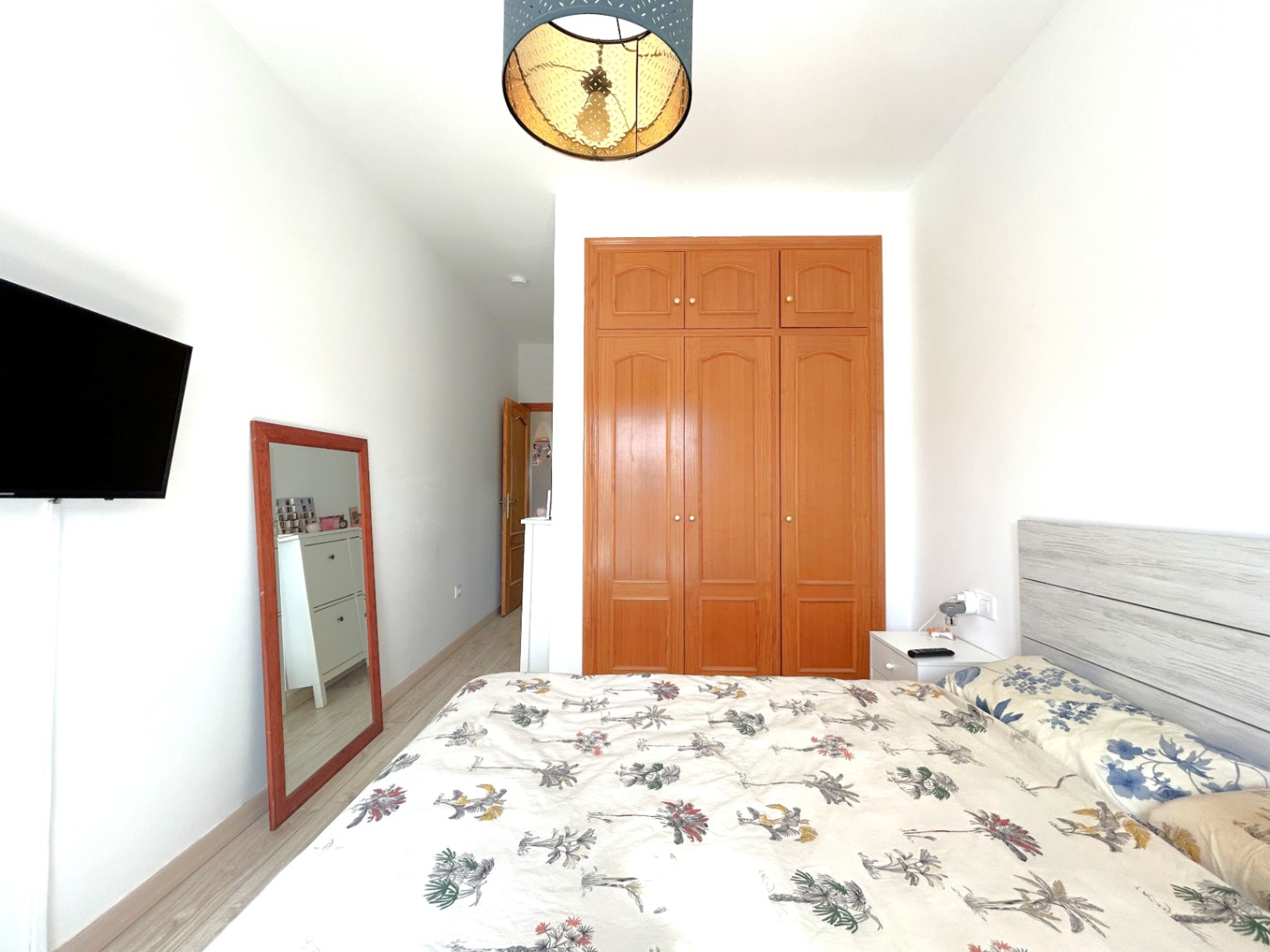 Dormitorio doble con armario empotrado de madera, suelos de tarima clara y televisión de pared. Incluye un espejo de cuerpo entero y una lámpara decorativa de techo.