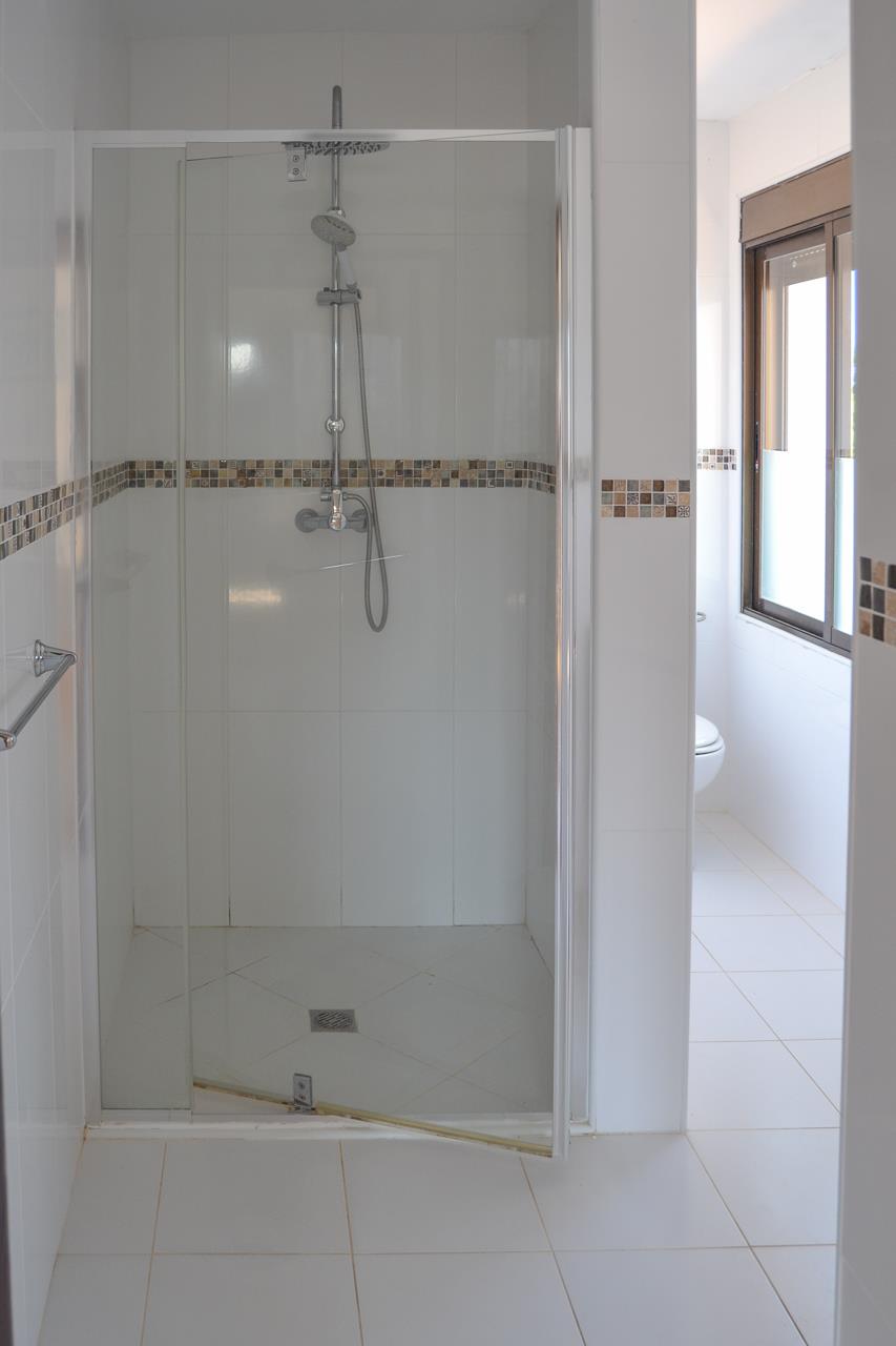 Cuarto de baño funcional con ducha de obra, mampara de cristal y azulejos blancos realzados por una cenefa decorativa de mosaico en tonos tierra.