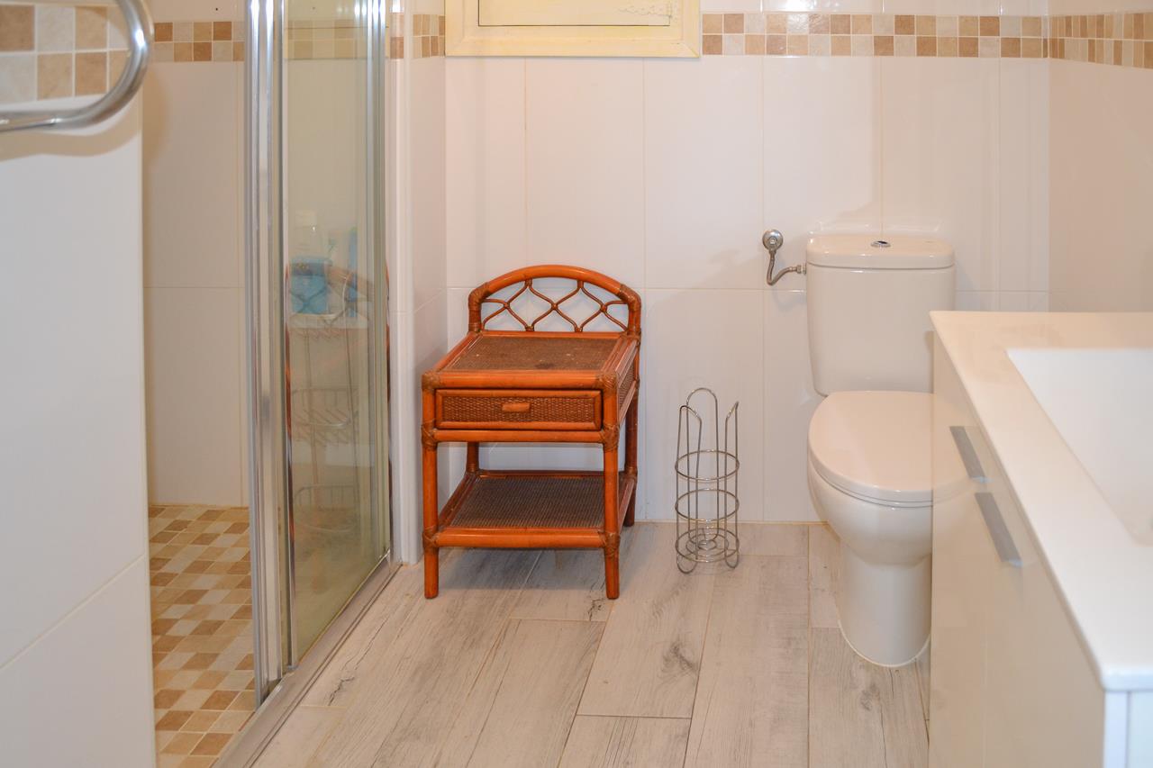 Cuarto de baño funcional con plato de ducha, mueble auxiliar de bambú, suelo de gres efecto madera y paredes alicatadas con cenefa de mosaico.