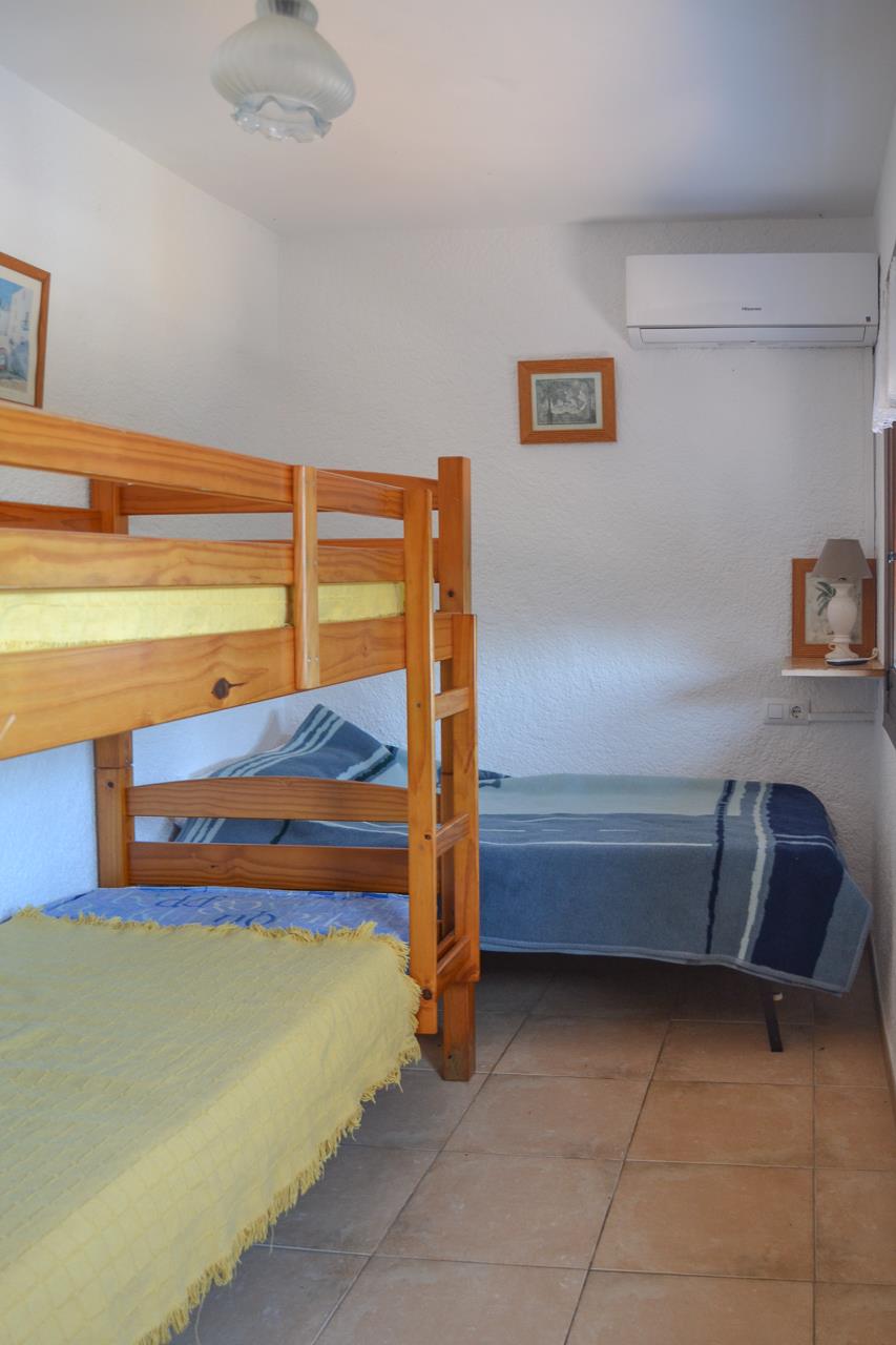 Dormitorio con literas de madera de pino y cama individual. Incluye aire acondicionado split, suelos cerámicos y paredes blancas de acabado rugoso.