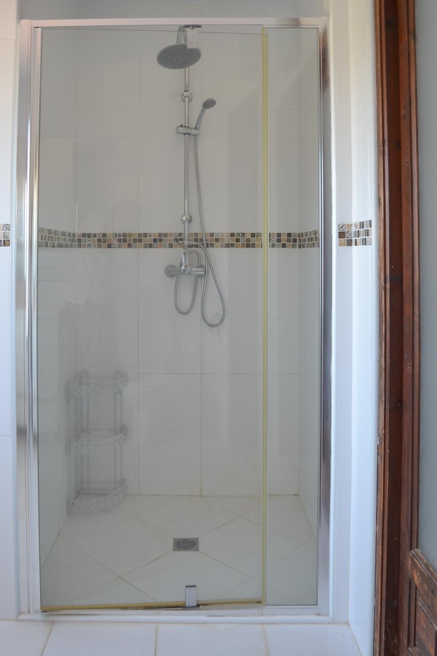 Ducha moderna con mampara de cristal, grifería de efecto lluvia y franja decorativa de mosaico en tonos tierra sobre azulejos blancos.
