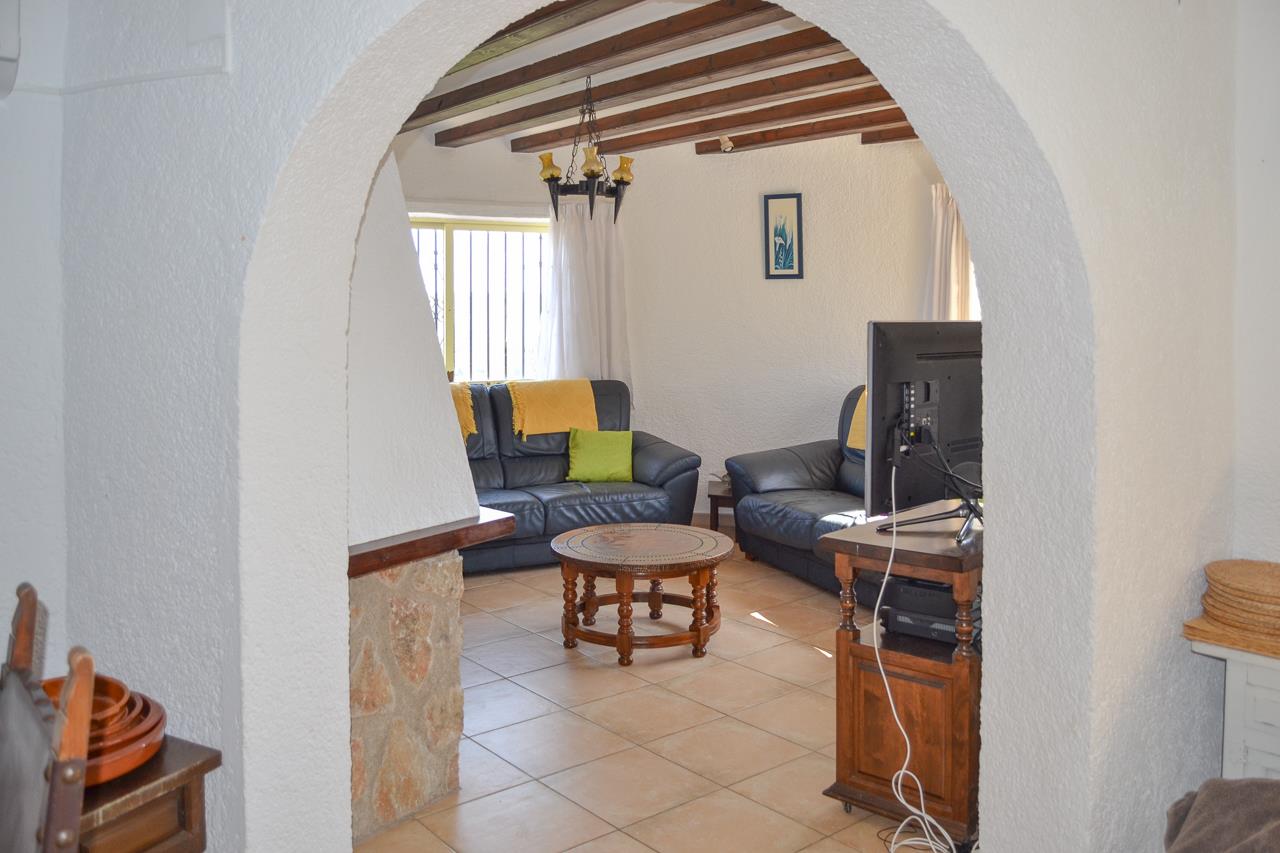 Salón rústico con techos de vigas de madera visto a través de un arco, equipado con sofás de cuero, chimenea de piedra y suelos cerámicos.