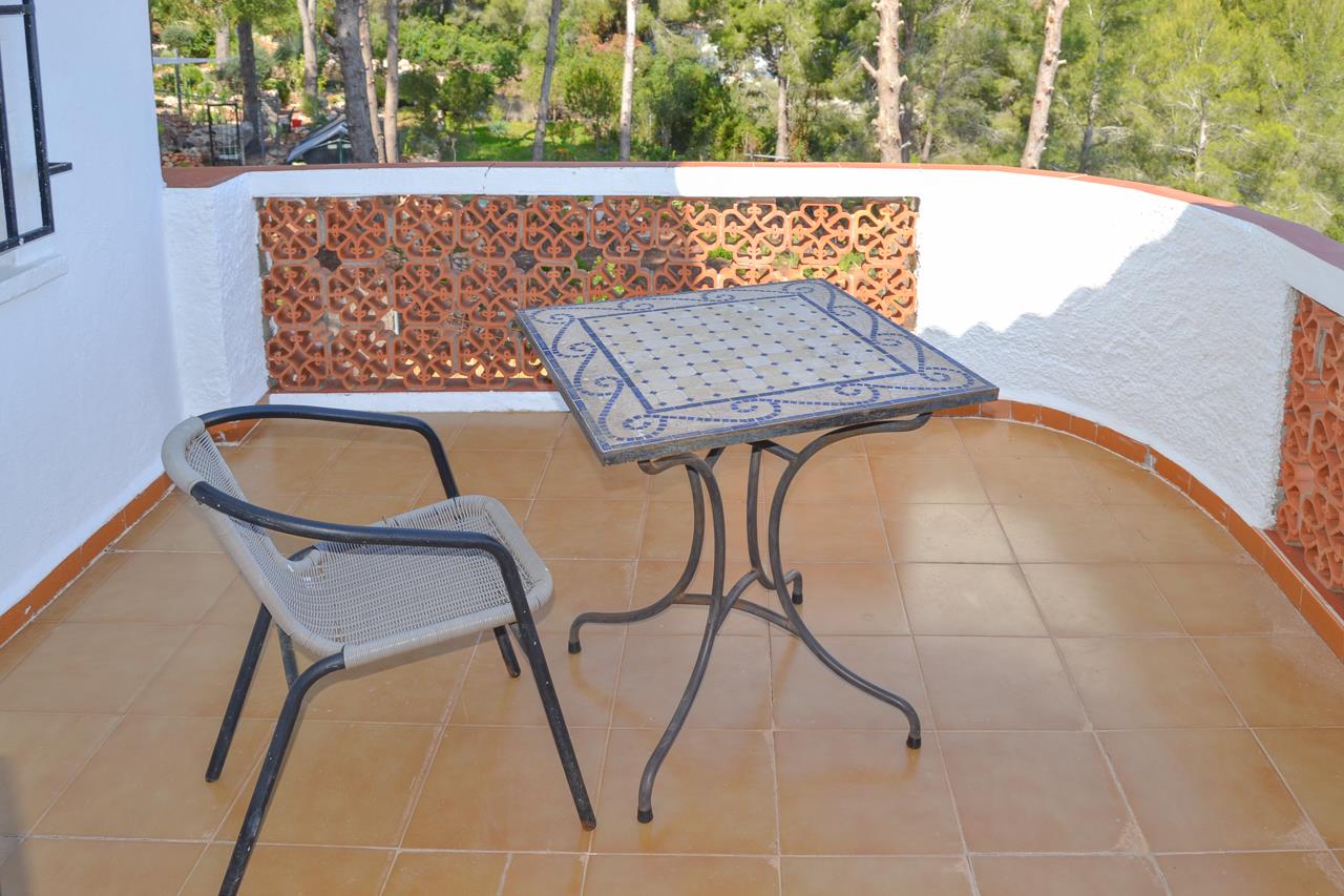 Terraza con suelo de gres, mesa de mosaico azul y silla de diseño, rodeada por una barandilla de celosía cerámica con vistas a la vegetación mediterránea.