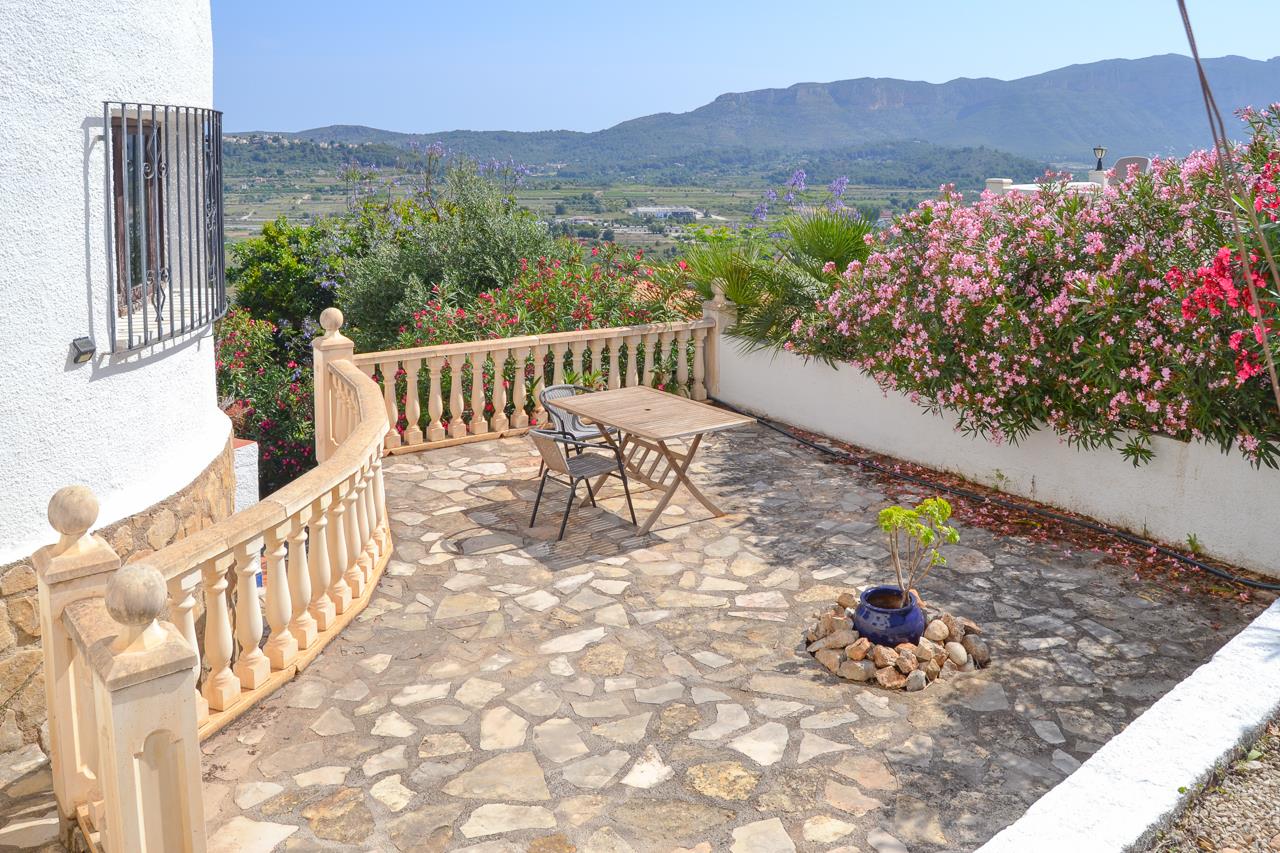 Terraza exterior con pavimento de piedra natural, balaustrada clásica y zona de comedor, ofreciendo vistas panorámicas al valle y las montañas circundantes.