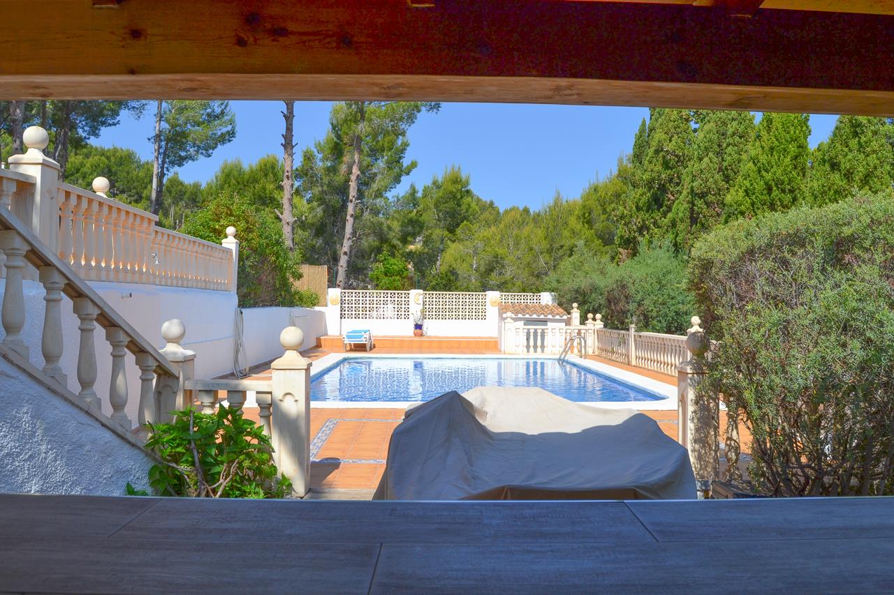 Vista desde la zona de barra hacia la piscina privada, rodeada de amplias terrazas de terracota, balaustradas blancas y vegetación mediterránea consolidada.