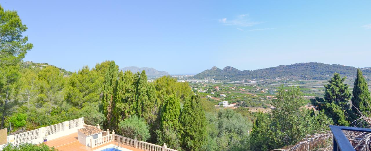 Vistas panorámicas despejadas hacia el valle y el mar Mediterráneo desde la terraza superior, con la zona de piscina y balaustrada de piedra en el nivel inferior.