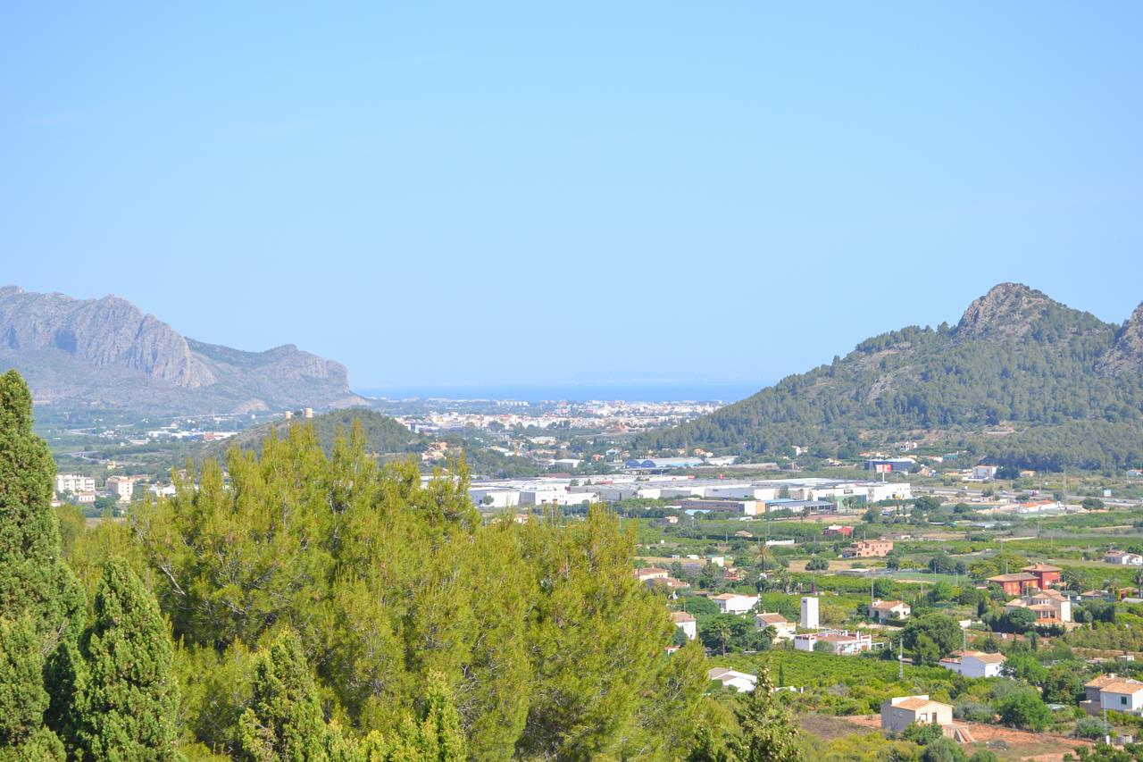 Vistas panorámicas despejadas hacia el valle y el mar Mediterráneo, enmarcadas por montañas y vegetación de pinos bajo un cielo despejado.
