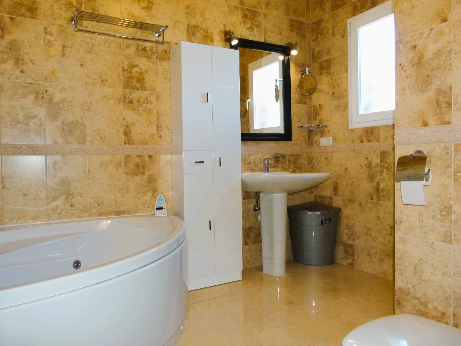 Cuarto de baño con bañera redonda, lavabo con pedestal y alicatado en tonos beige.