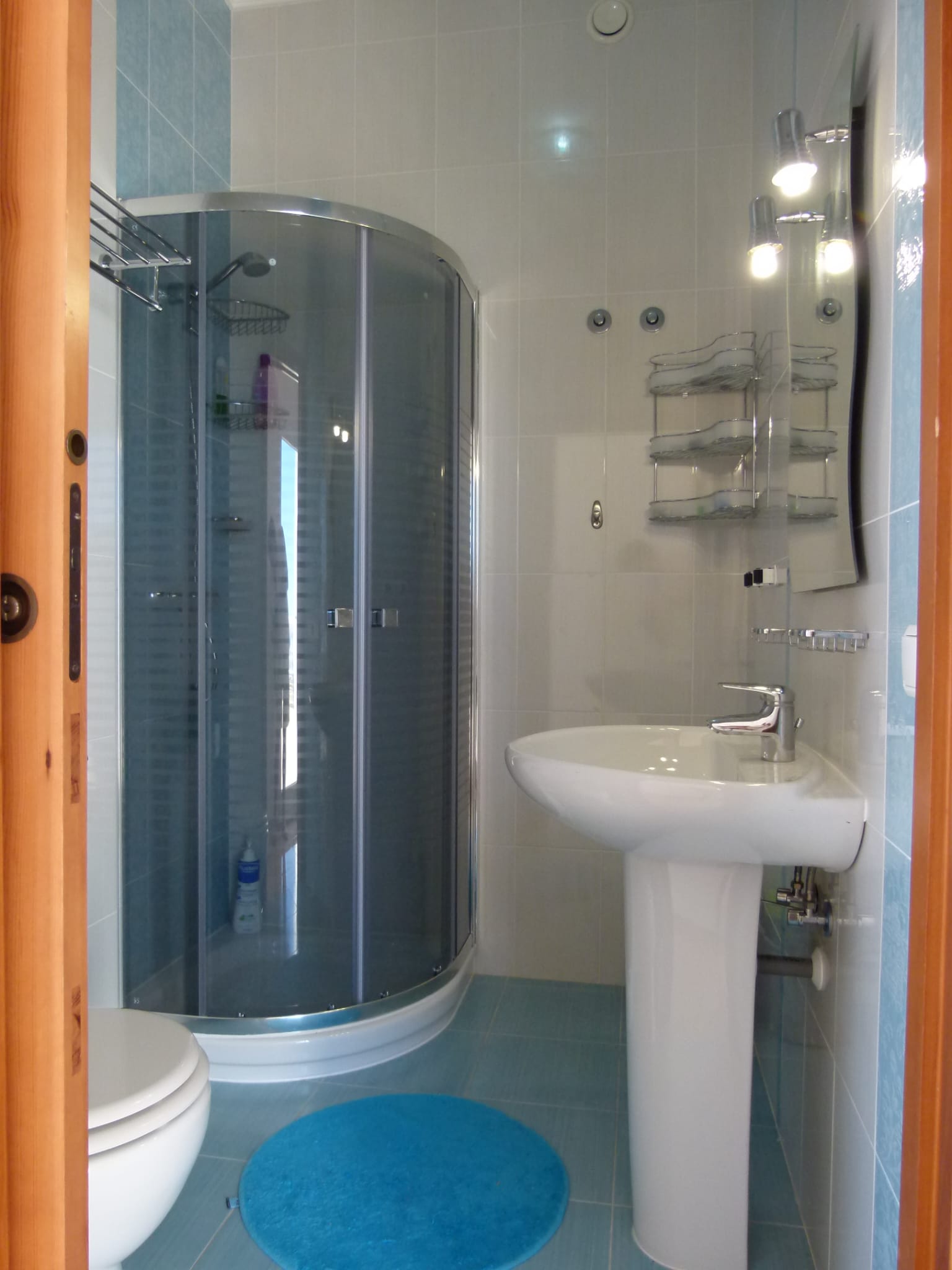 Detalle de baño con ducha esquinera y lavabo pedestal, azulejos azules.