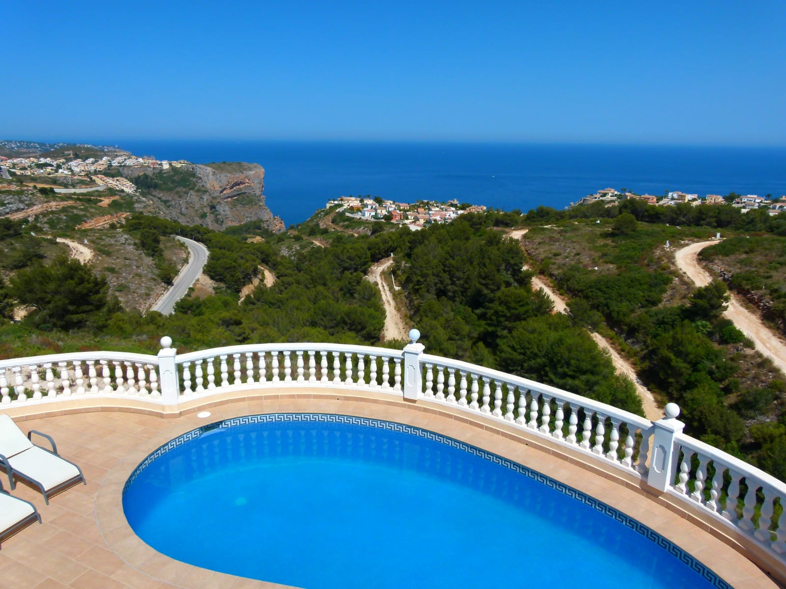 Vista de la piscina privada con barandilla blanca y vistas panorámicas a la costa y vegetación.
