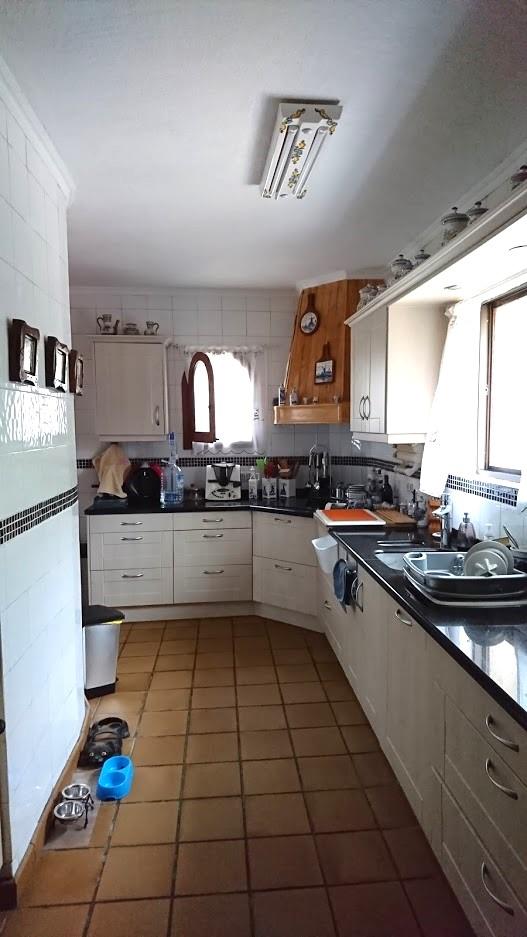 Cocina independiente con armarios blancos, encimera oscura y suelos de gres rústico. Destaca la campana extractora de madera y el alicatado con cenefa decorativa.