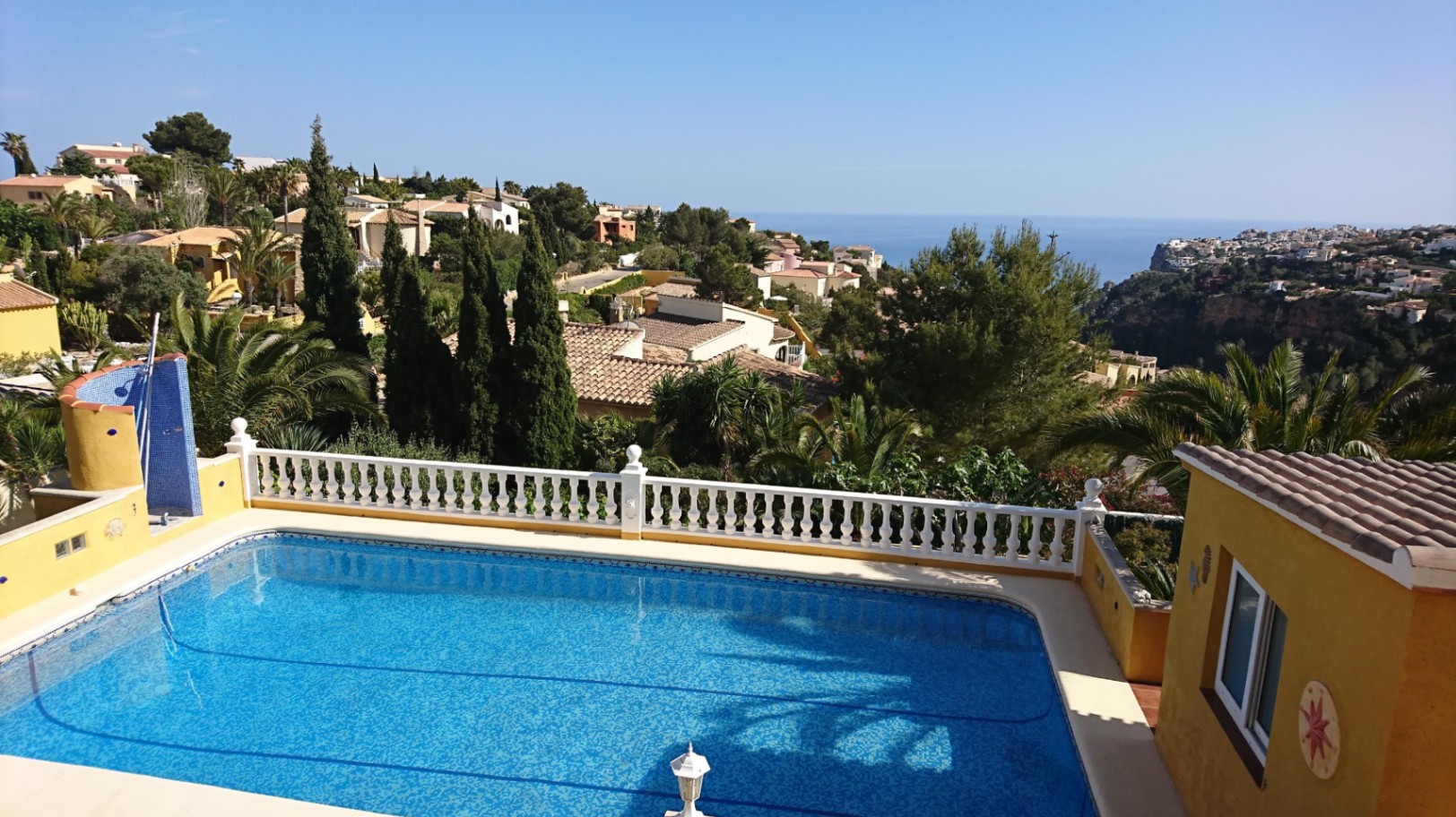 Piscina rectangular con balustrada blanca y ducha exterior, ofreciendo vistas despejadas al mar Mediterráneo y al entorno residencial de Cumbre del Sol.